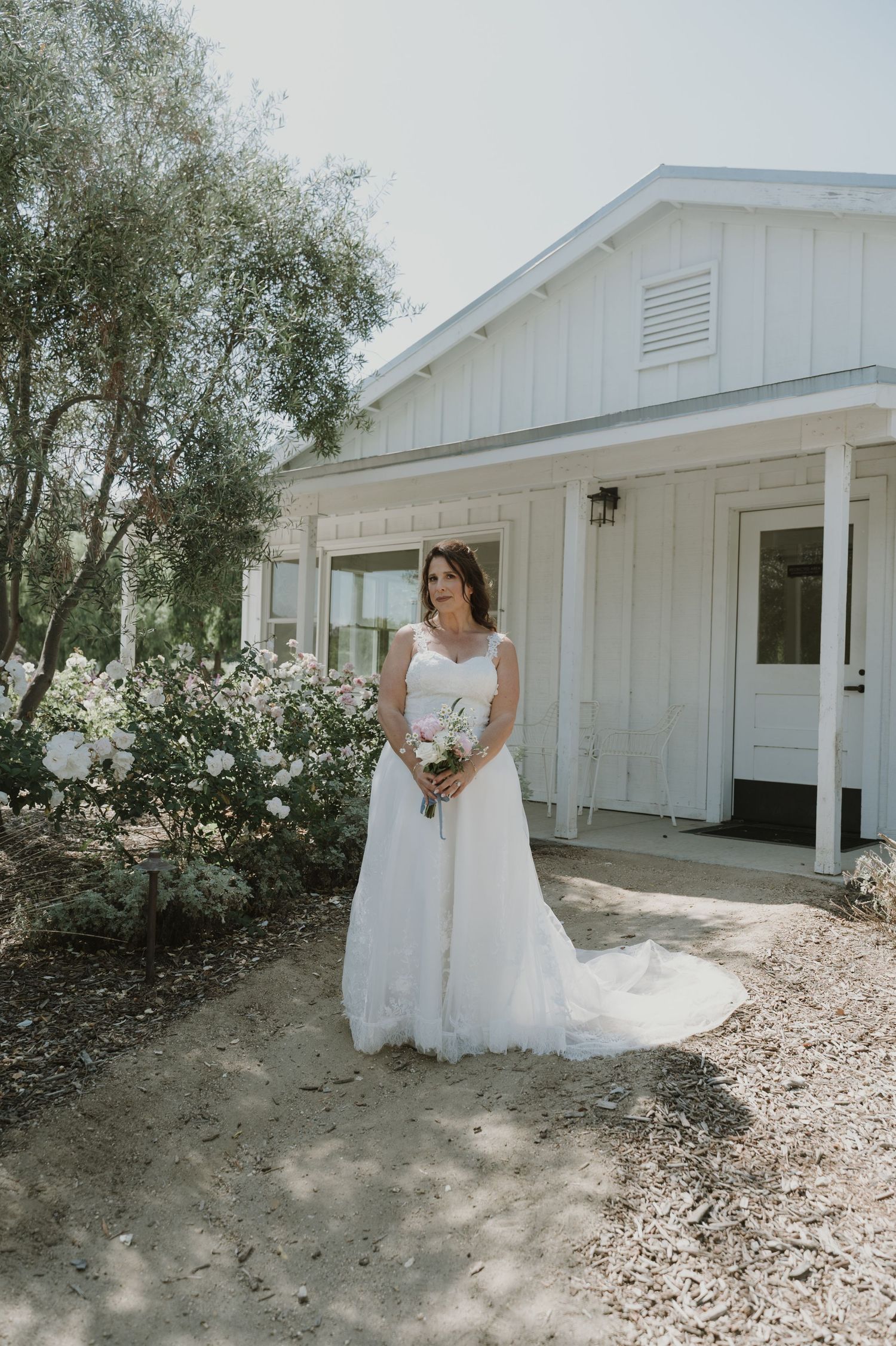 White wedding venue exterior with rustic charm surrounded by trees and gravel paths.