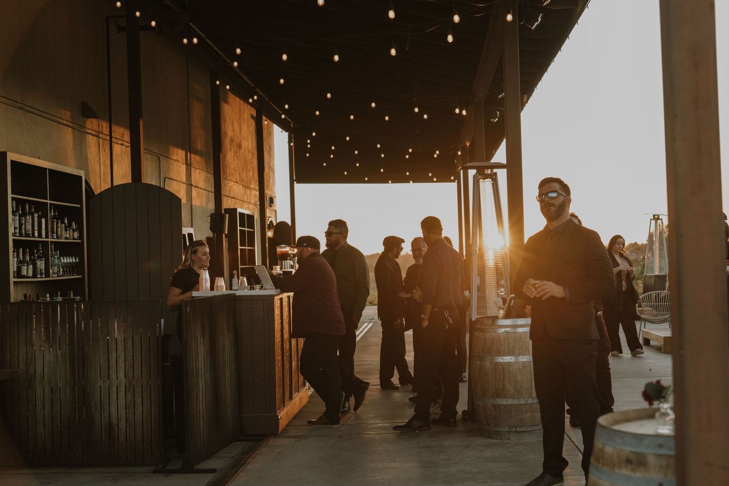 Wedding guests mingle during golden hour under twinkling string lights at outdoor reception.