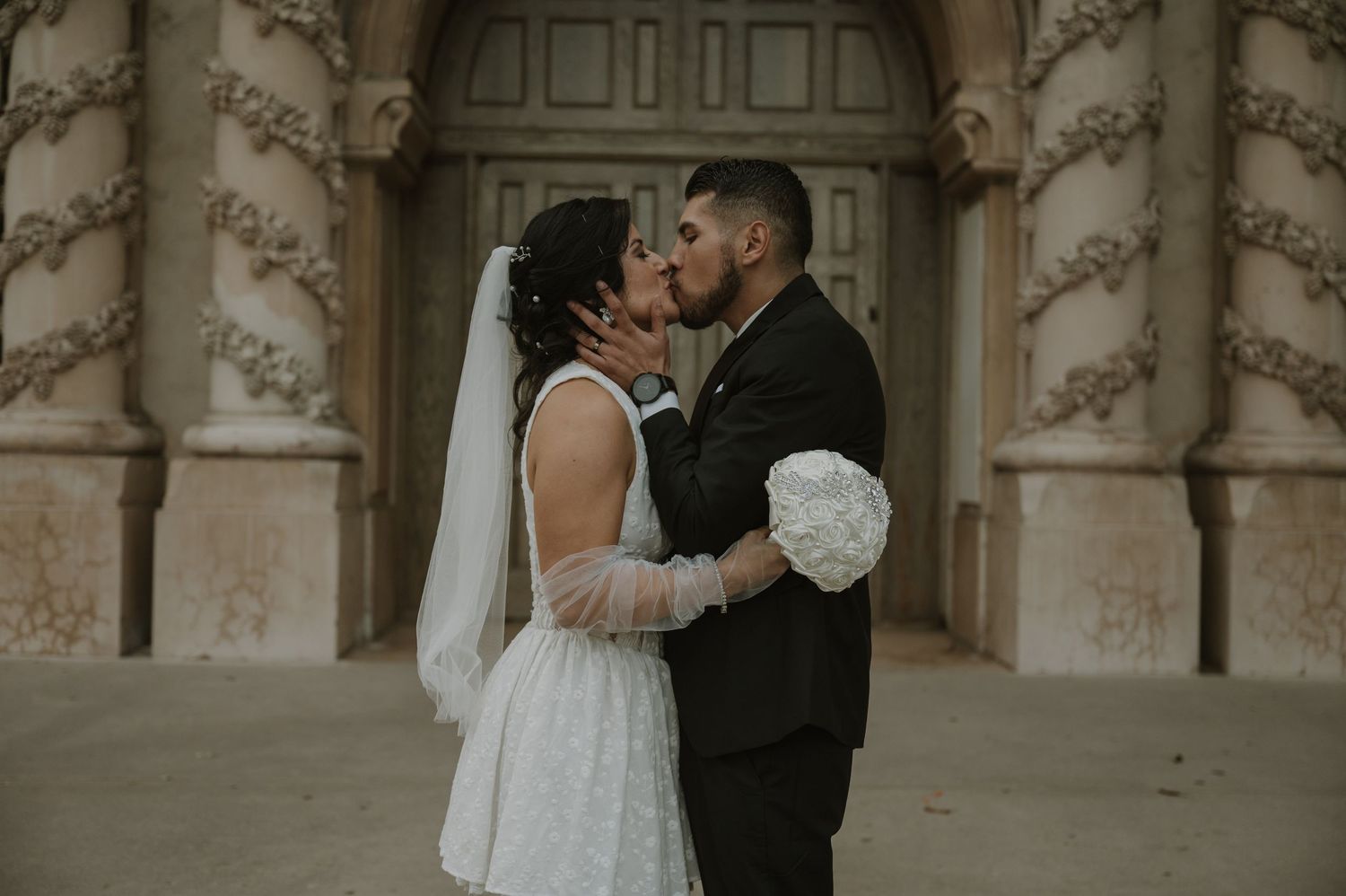 Elegant wedding couple embraces in front of an ornate architectural backdrop.