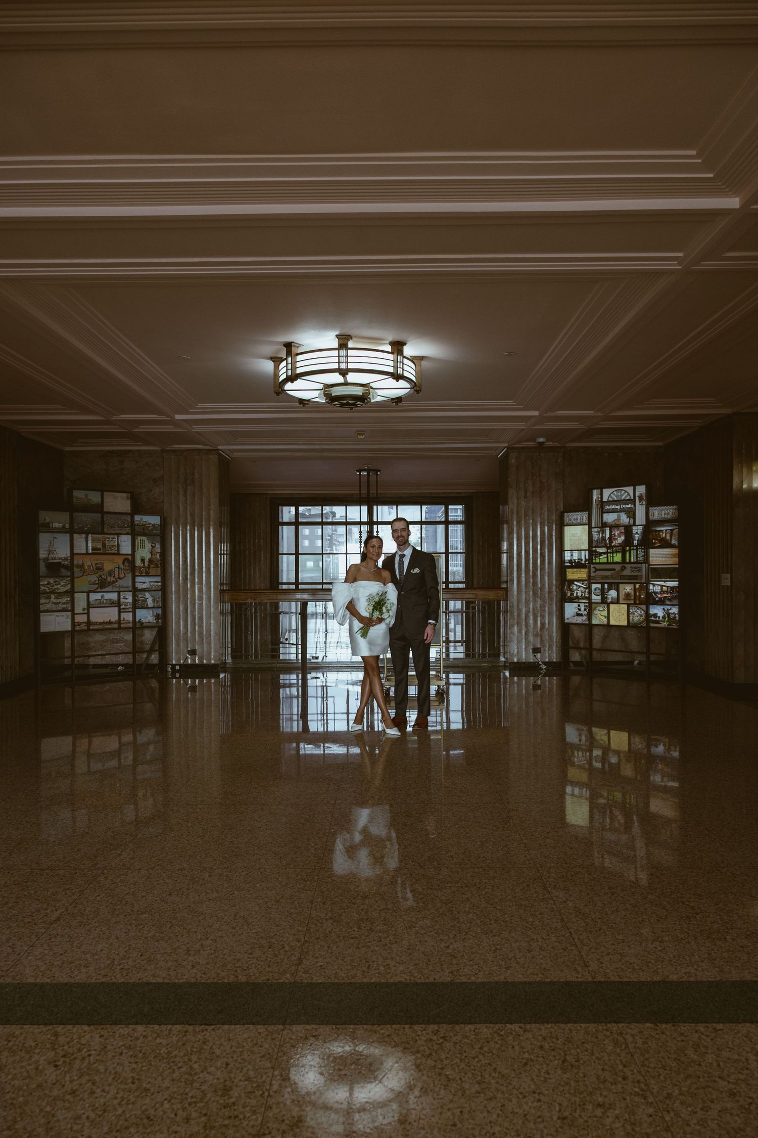 Long empty corridor with reflective floors and ceiling lights creating moody atmosphere.