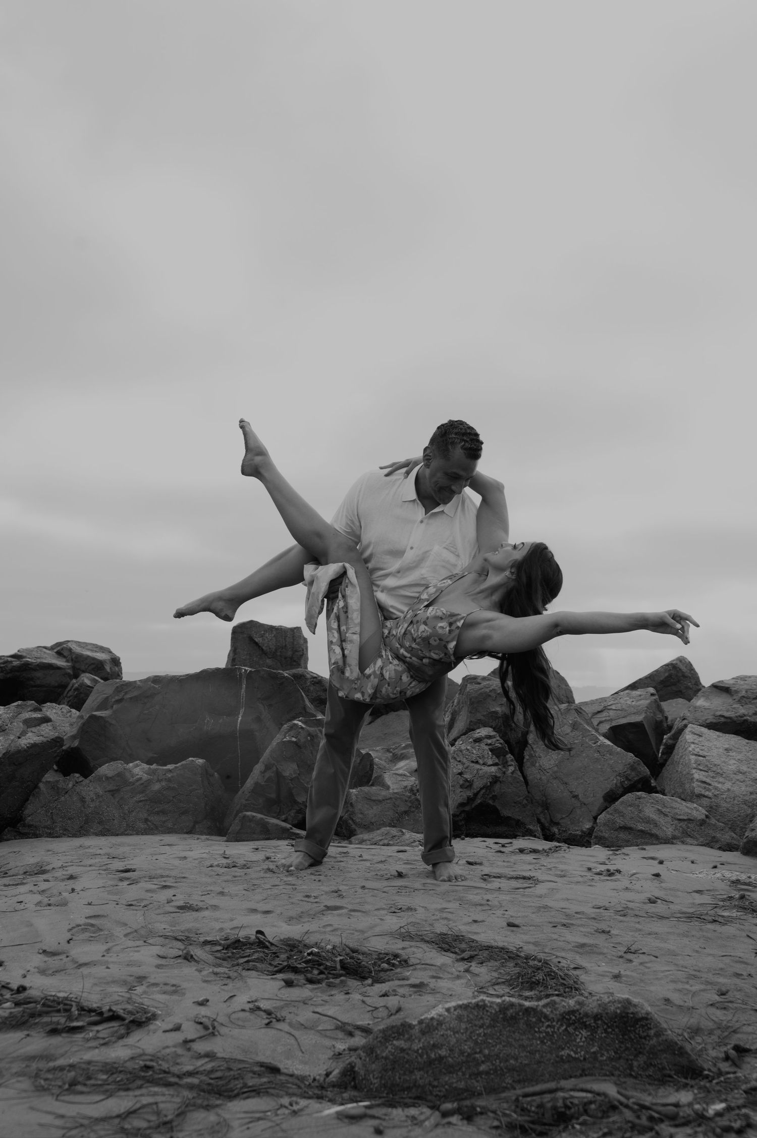 Artistic black and white photo of a couple posing on coastal rocks.
