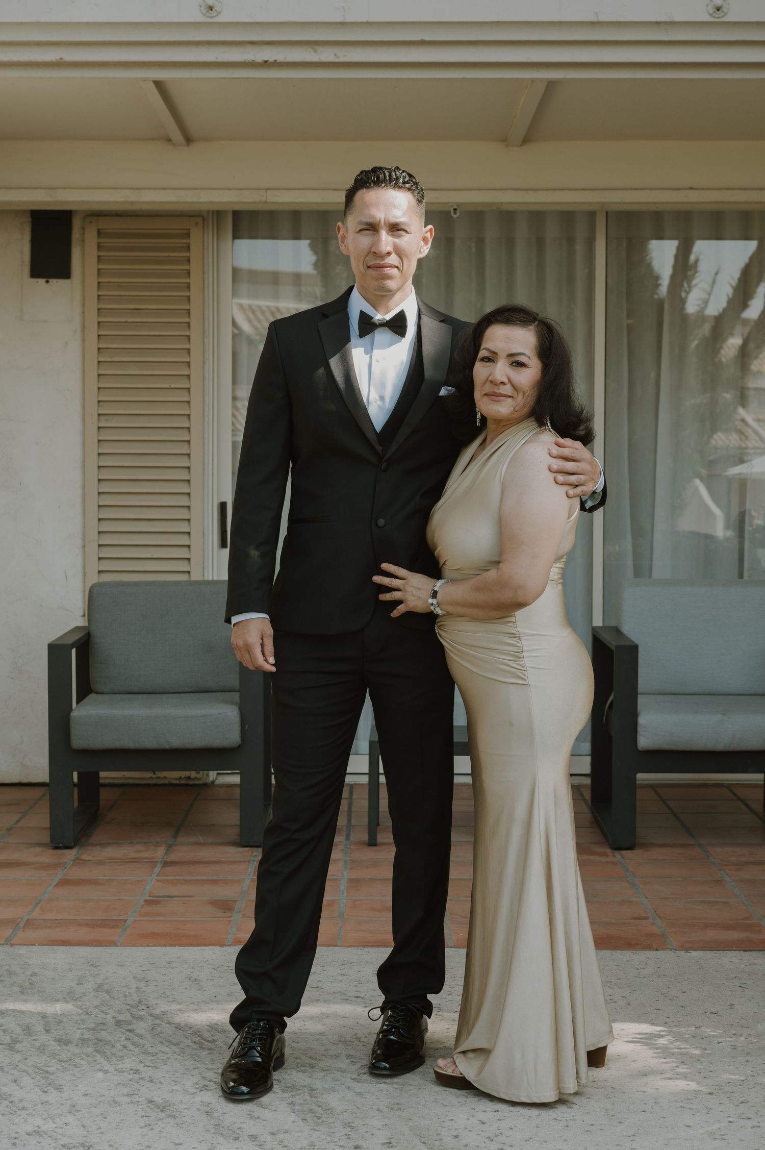 Formal couple in evening wear posing together on outdoor patio.