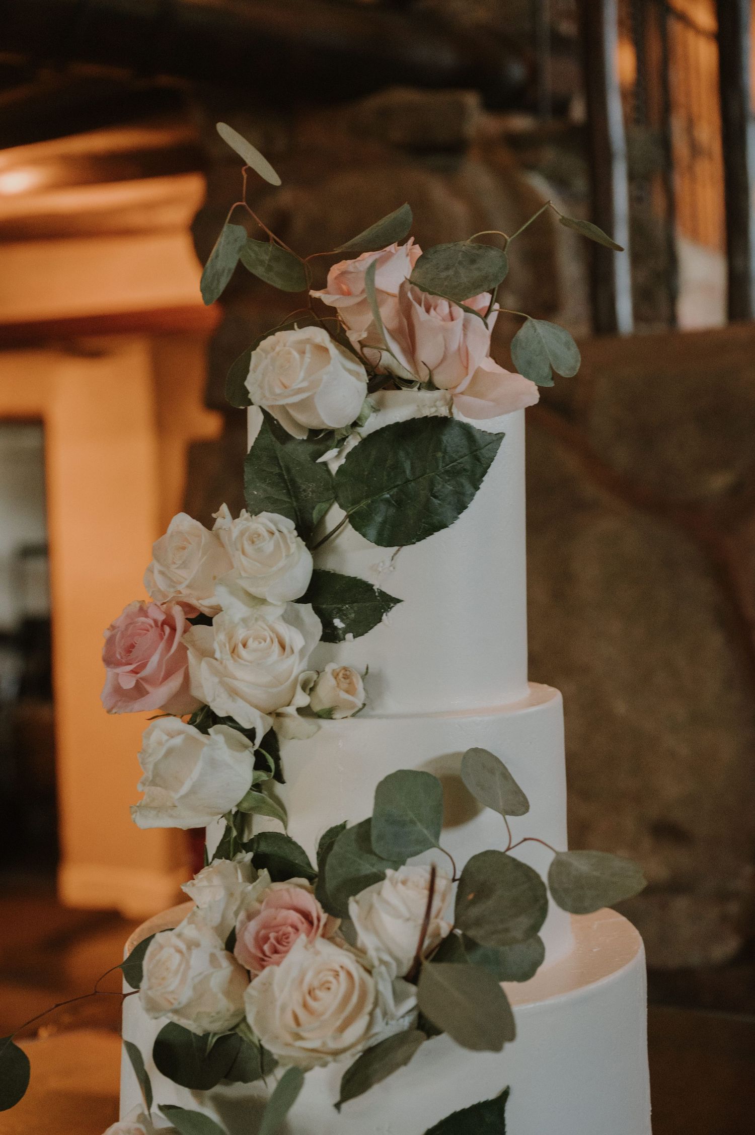 Elegant three-tier white wedding cake adorned with cascading pink and cream roses and eucalyptus greenery.
