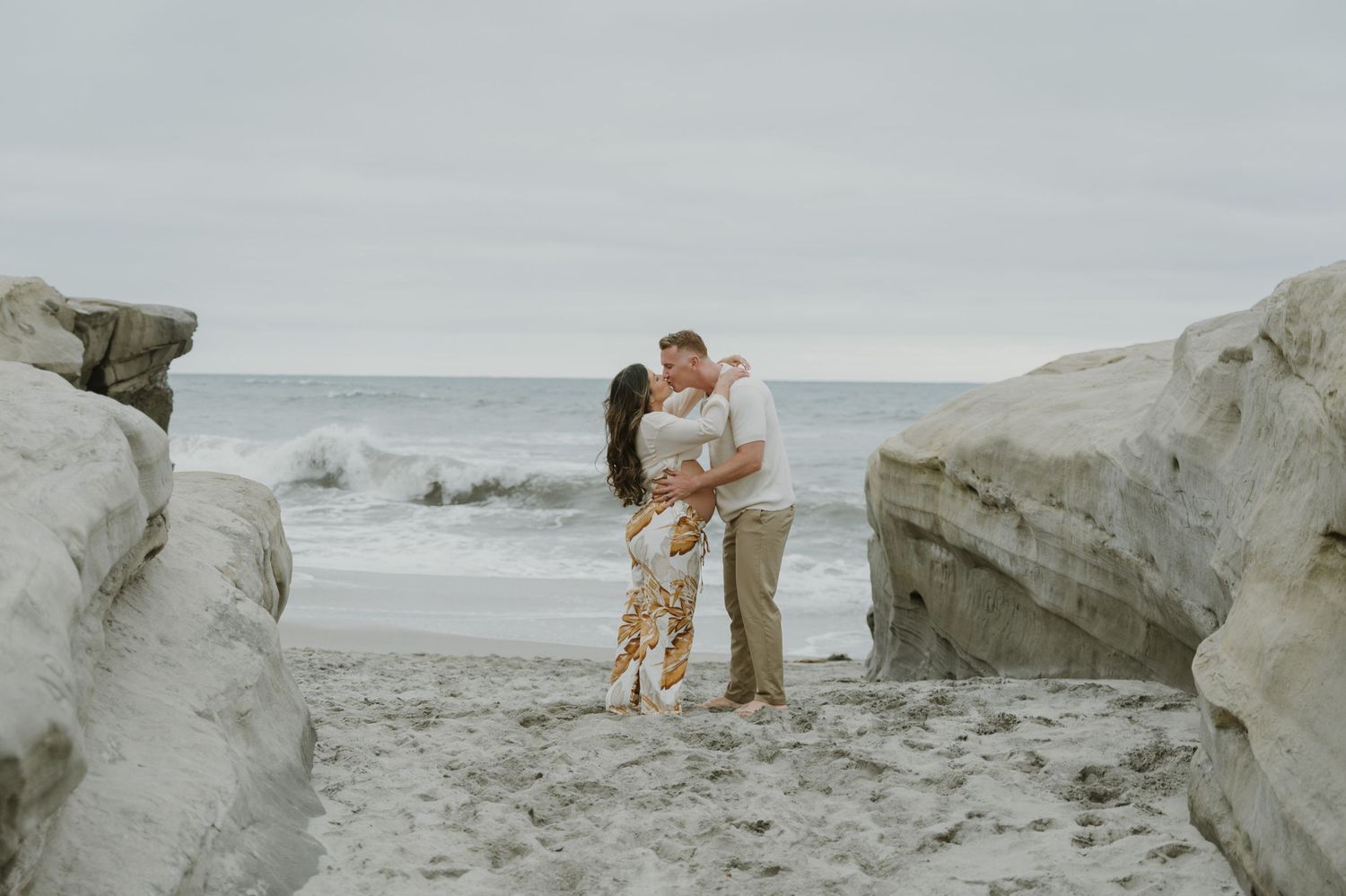 A romantic moment captured between rocks on a misty beach.