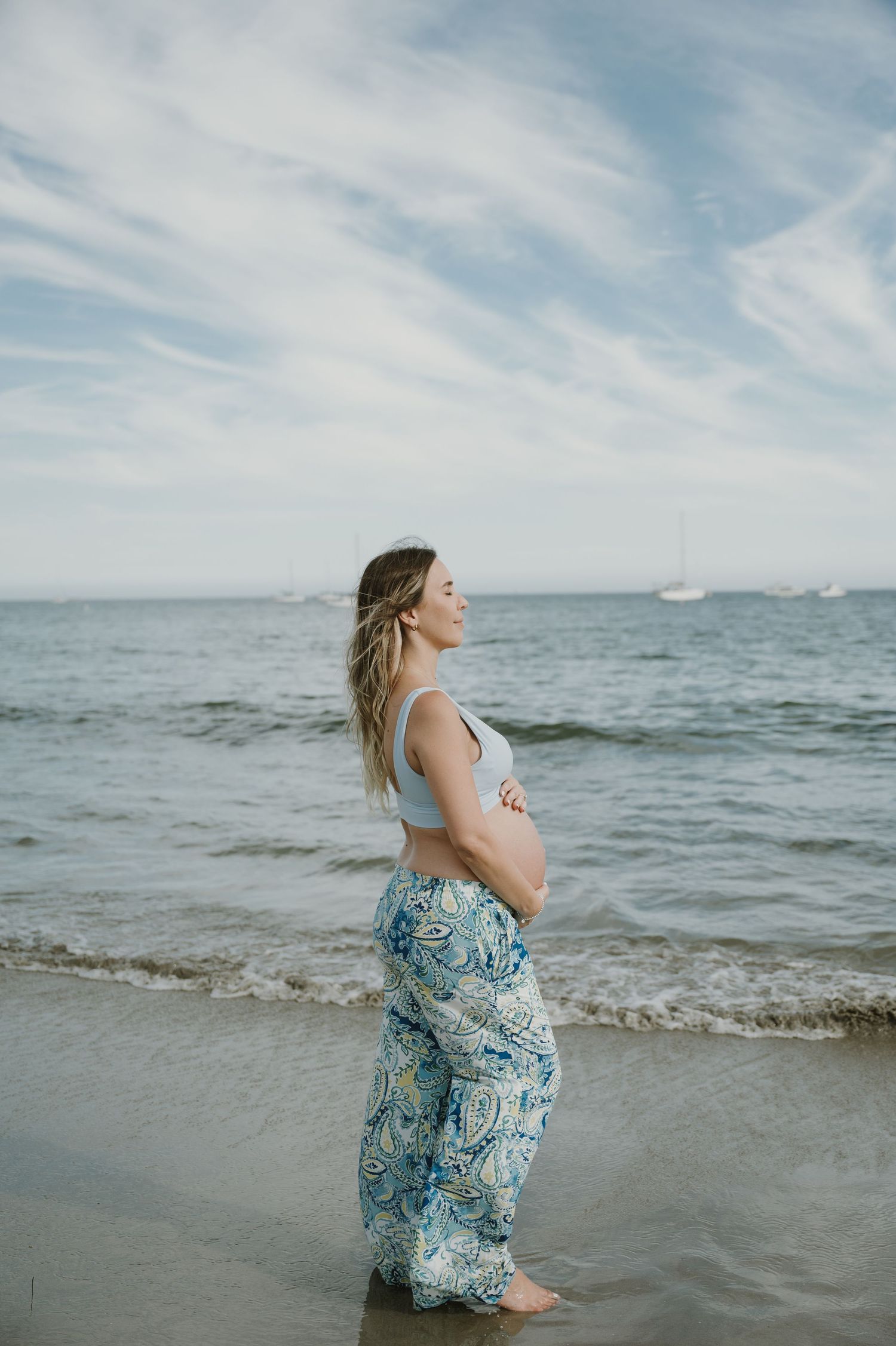 A flowing blue dress catches the ocean breeze as waves roll onto the beach.