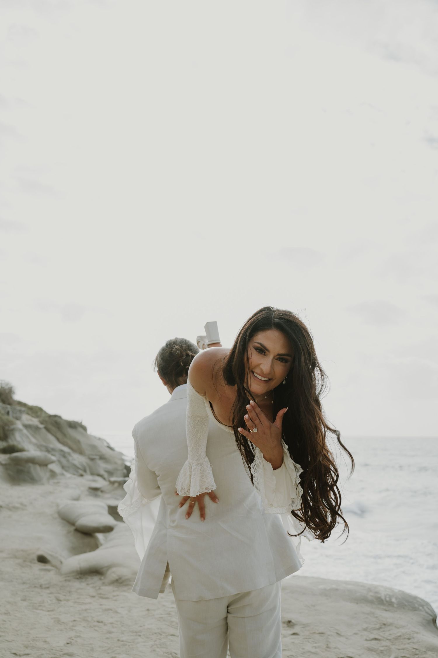 A bride in a white dress laughs joyfully during a beach photoshoot.