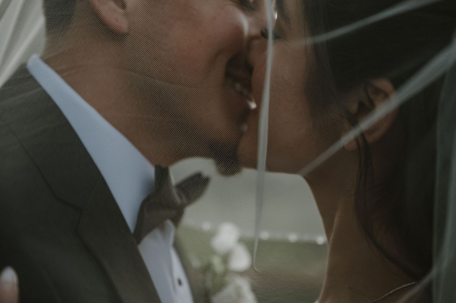 Artistic close-up shot of couple sharing romantic moment through sheer wedding veil.