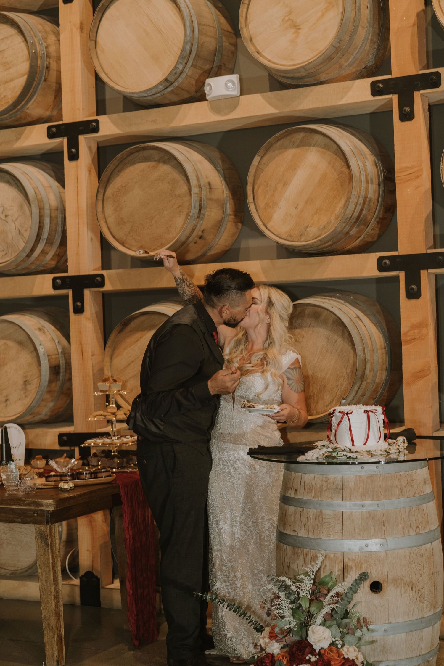Intimate wedding cake cutting moment in front of stacked wine barrels.