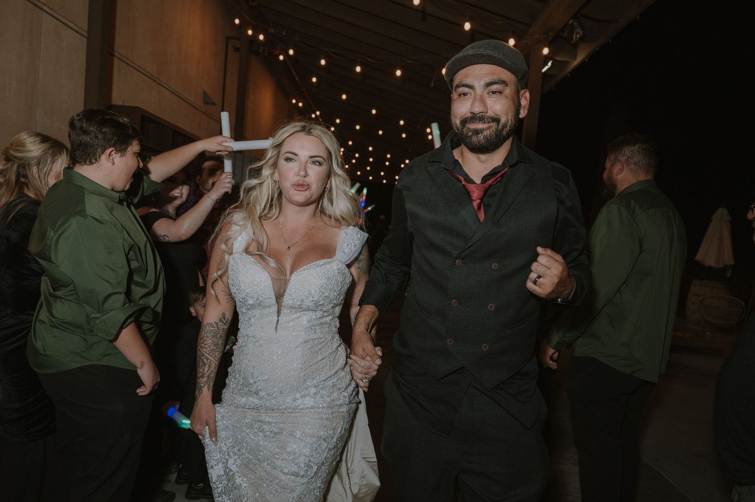 Wedding party dancing and celebrating under warm string lights at an evening reception.