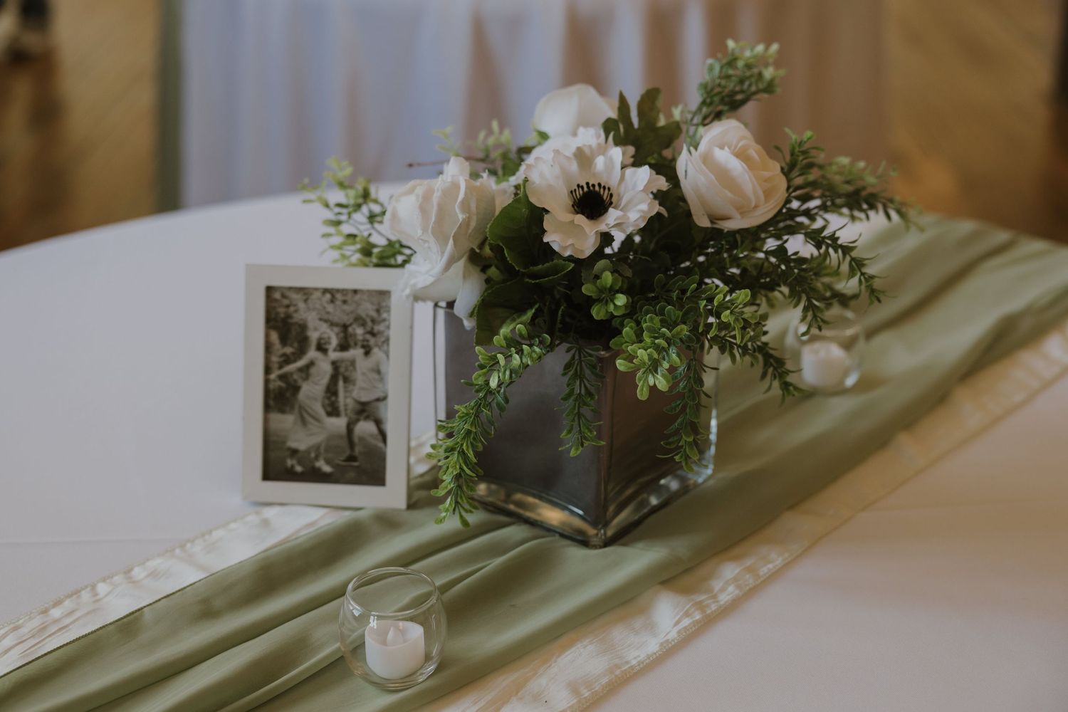 Elegant wedding reception tables decorated with white linens, floral centerpieces and soft drapery in a banquet hall.