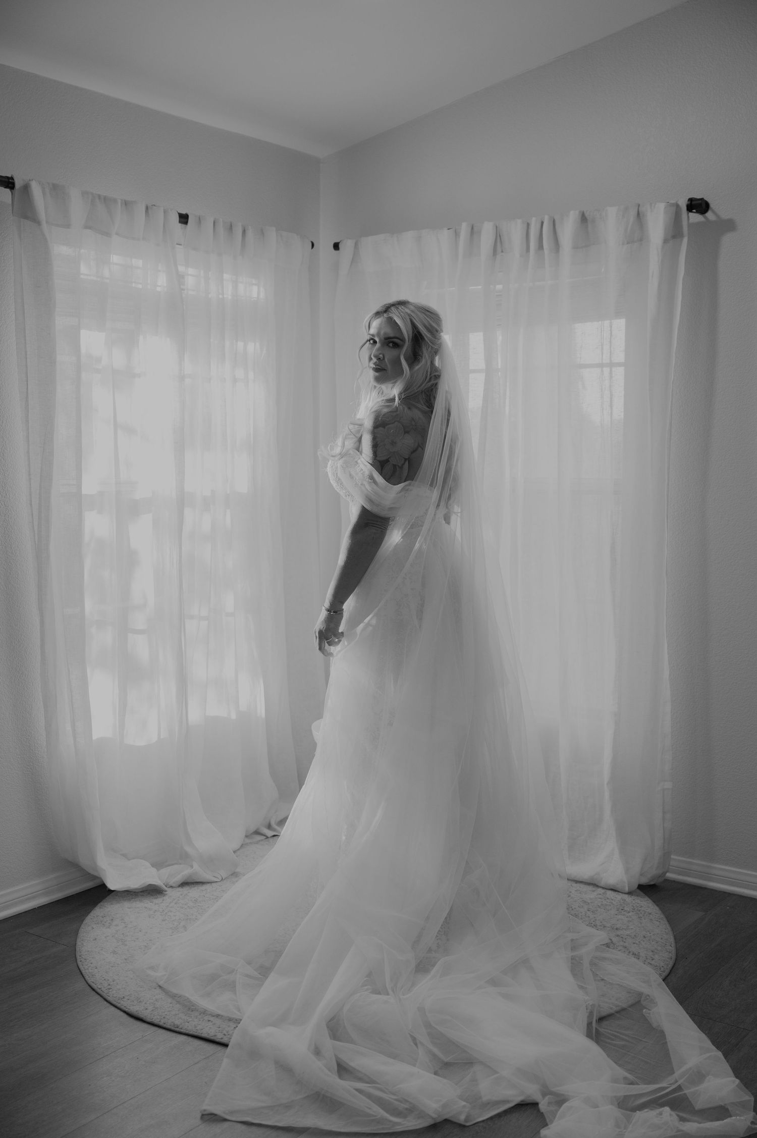 Ethereal black and white photograph of flowing wedding dress against sheer curtains.