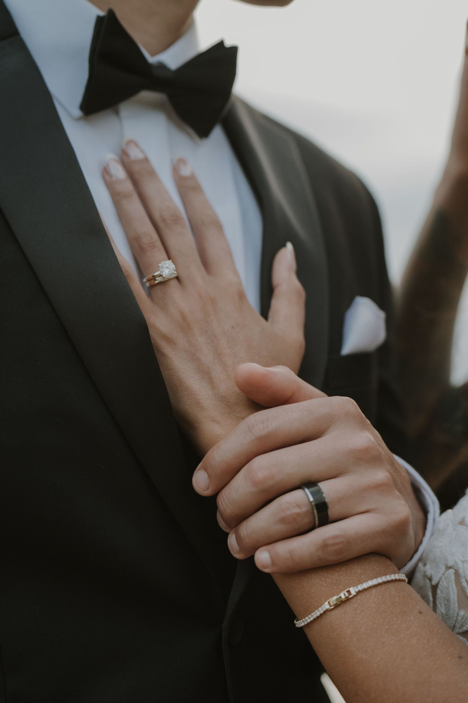 Close-up of hands wearing wedding rings and formal attire showing romantic details.