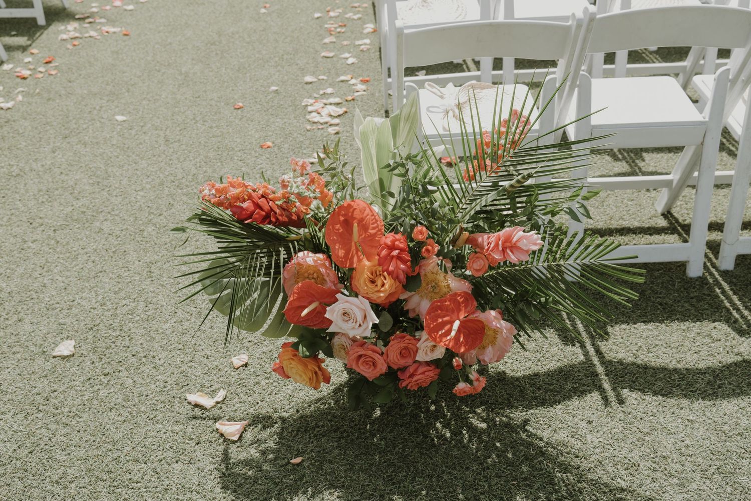 Coral and pink floral arrangements line the wedding ceremony aisle.