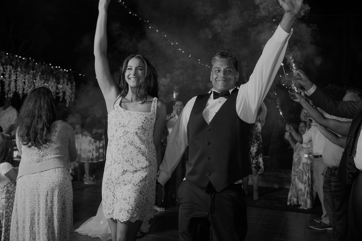 Black and white photo of a joyful couple raising their hands at a wedding reception celebration.