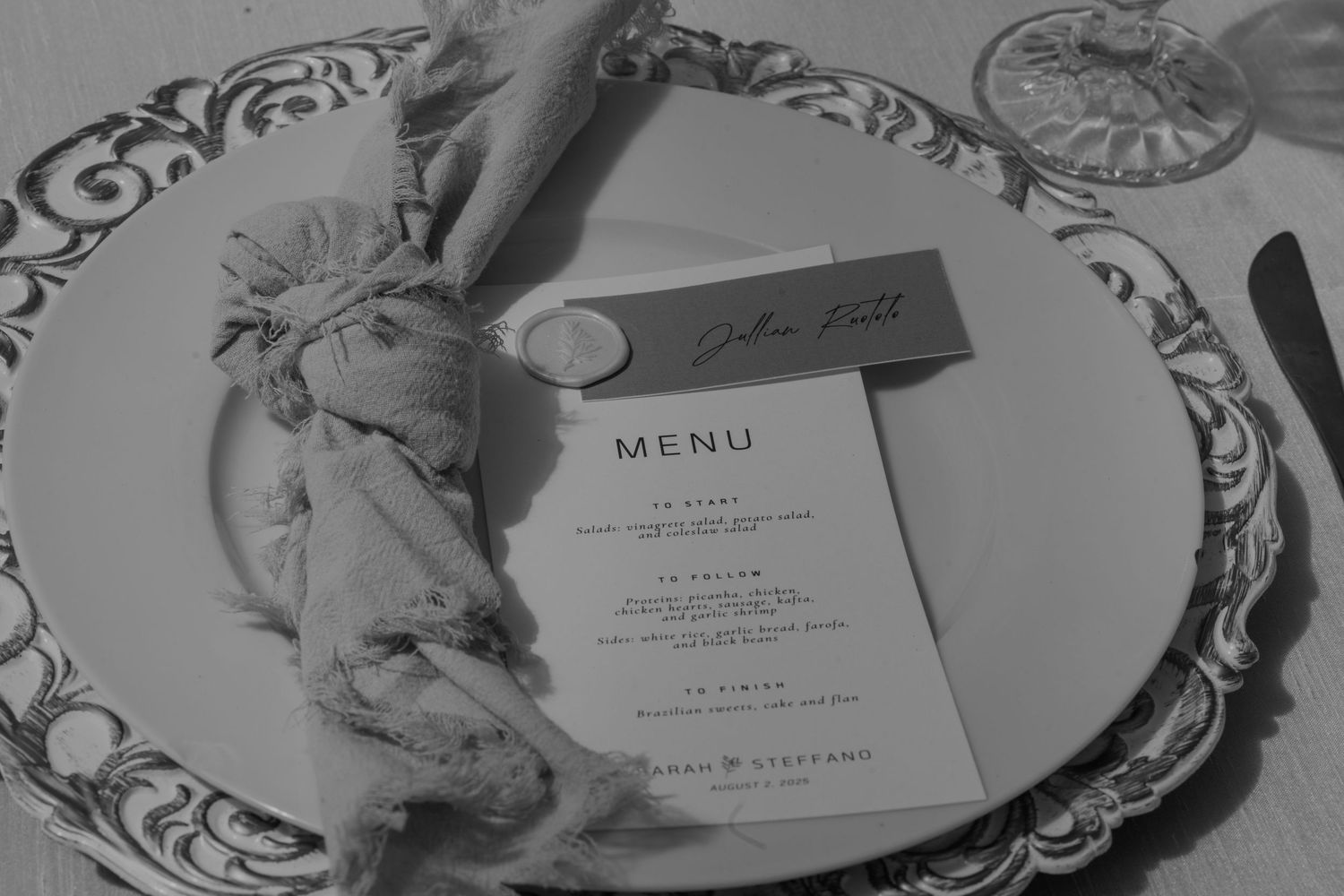Elegant wedding place setting with a printed menu card, name card, and decorative napkin on an ornate white plate.