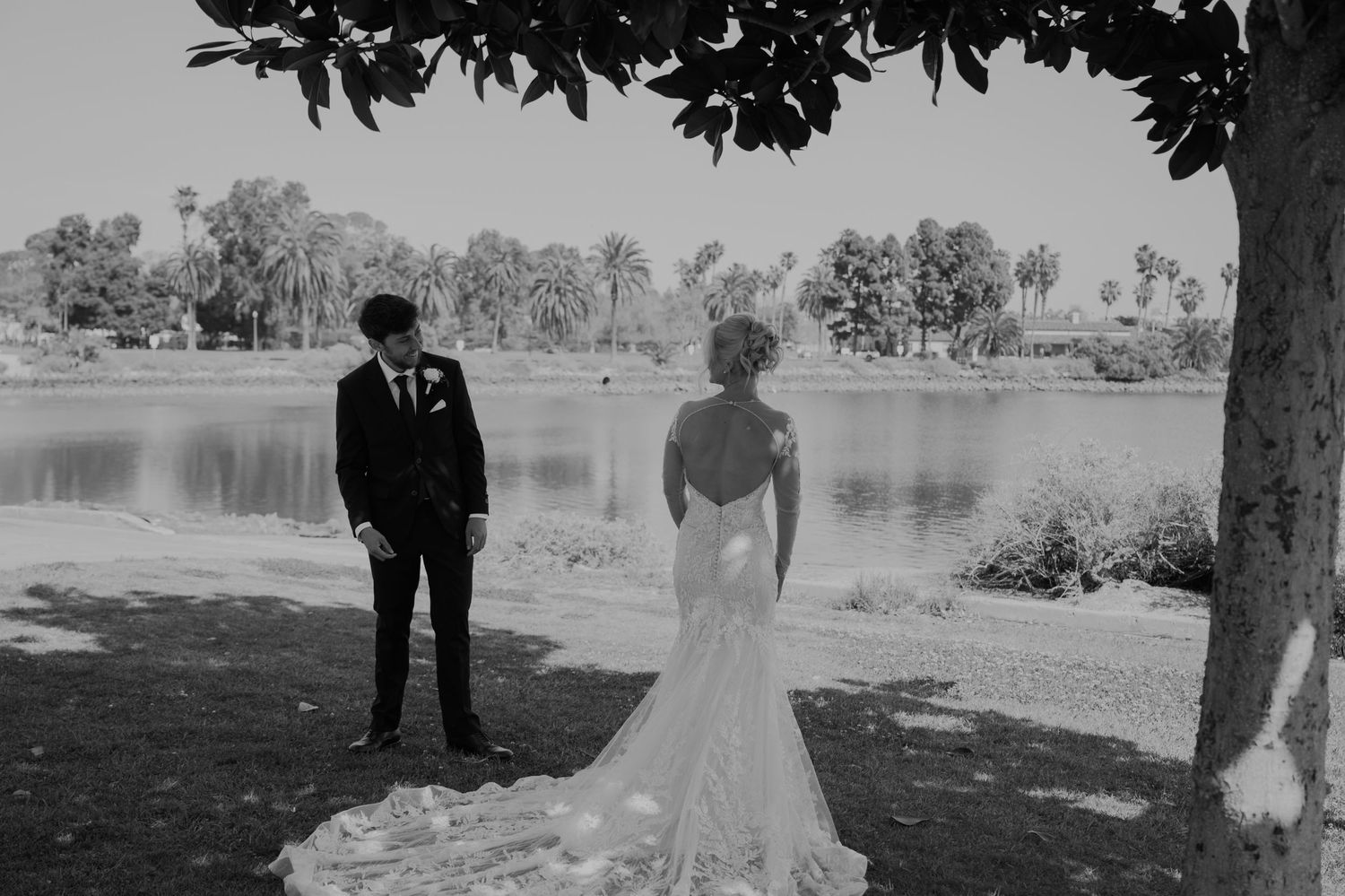 Black and white photo of bride and groom sharing a first look moment by a serene lake surrounded by palm trees.