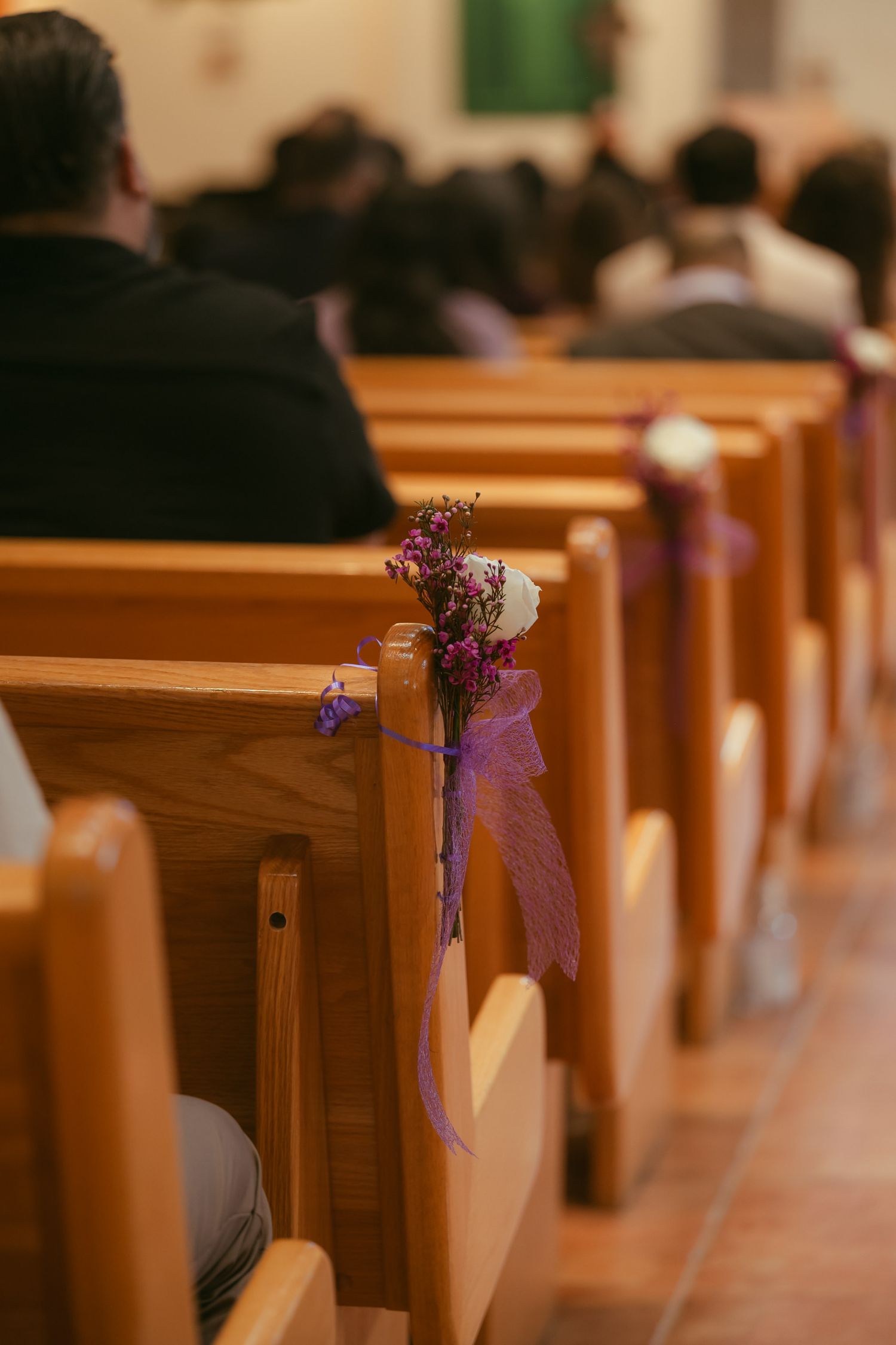 Church pews decorated with purple flowers and ribbon boutonnieres for a wedding ceremony.