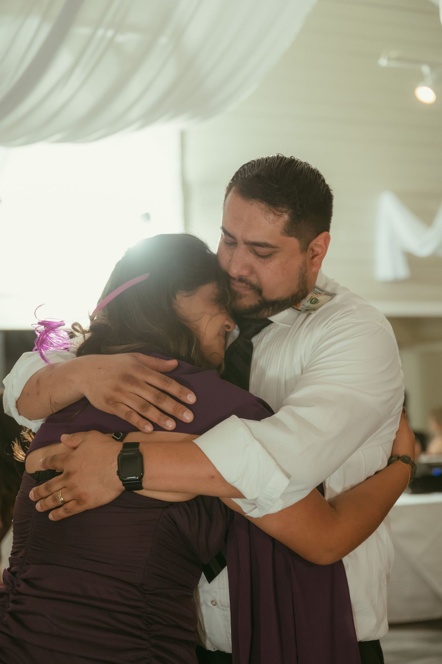 Emotional groom shares a heartfelt hug with a woman in a purple dress during wedding reception dance.
