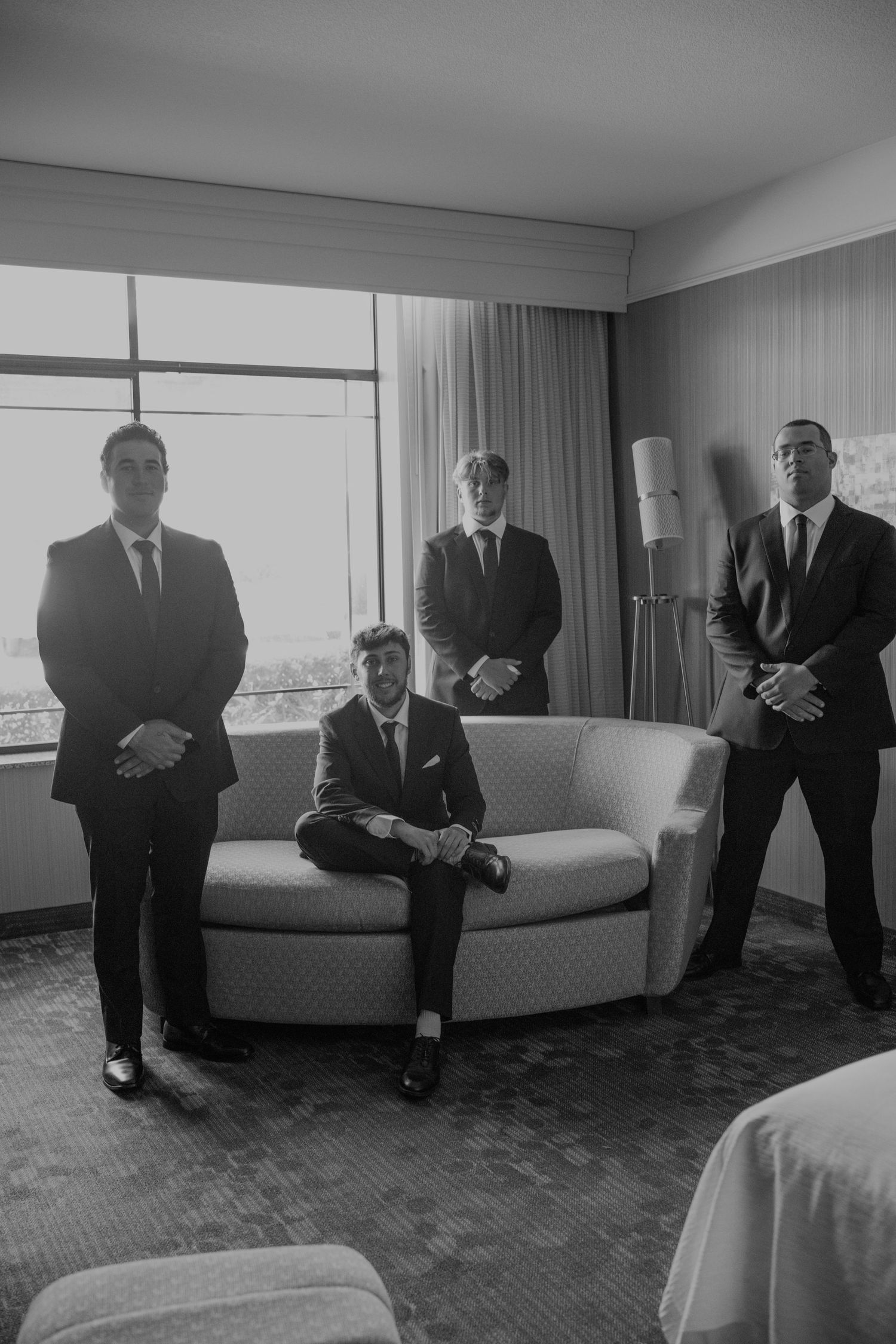 Black and white photo of groom and groomsmen in suits posing in hotel room before wedding.