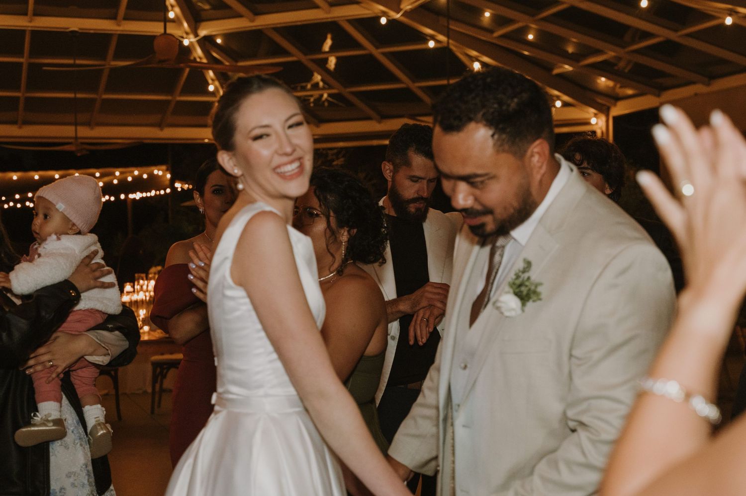 Smiling bride and groom holding hands dancing joyfully with guests at wedding reception.