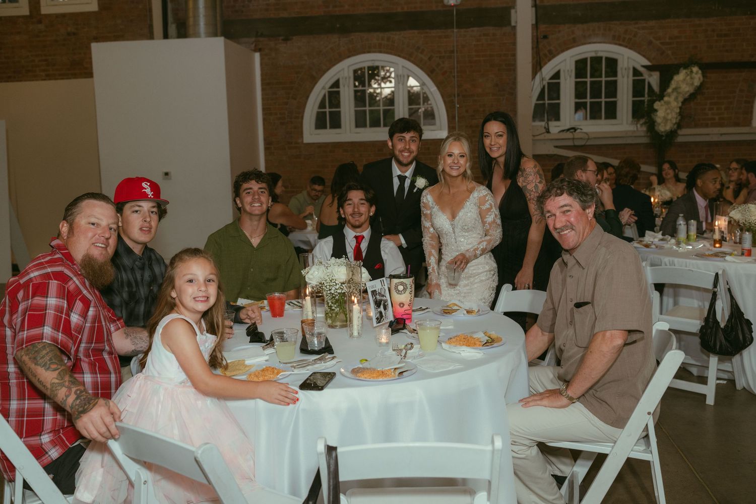 Wedding guests smiling at round table during reception celebration in brick venue.