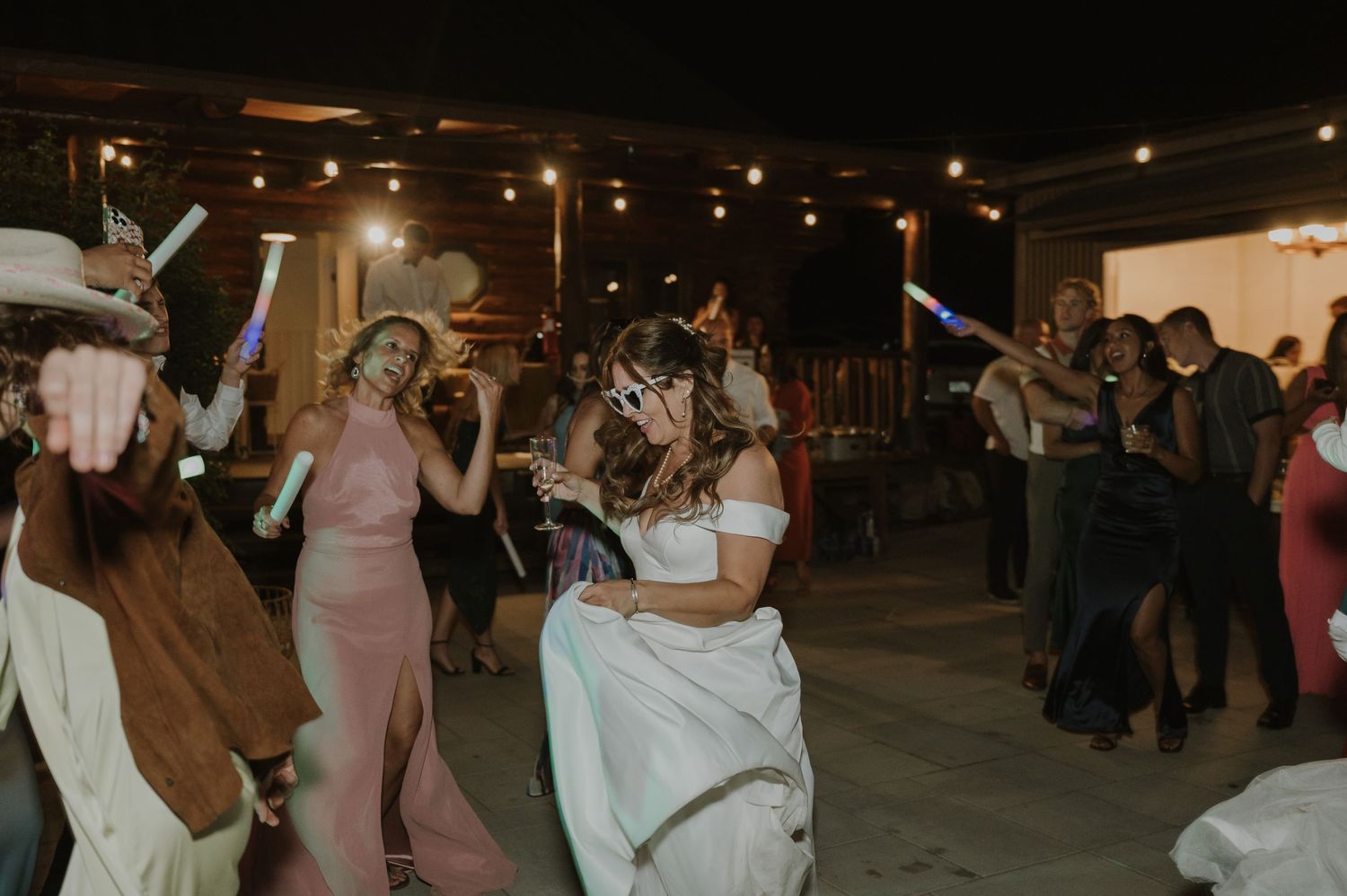 Guests dancing joyfully at an outdoor wedding reception under string lights at night.