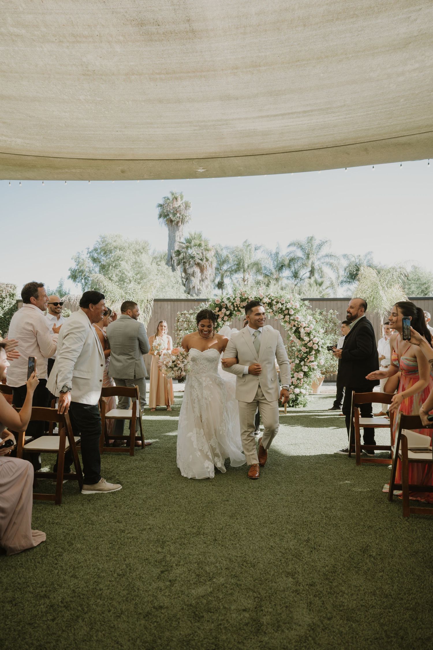 Bride and groom walk down the aisle at an outdoor wedding ceremony under a tent canopy.