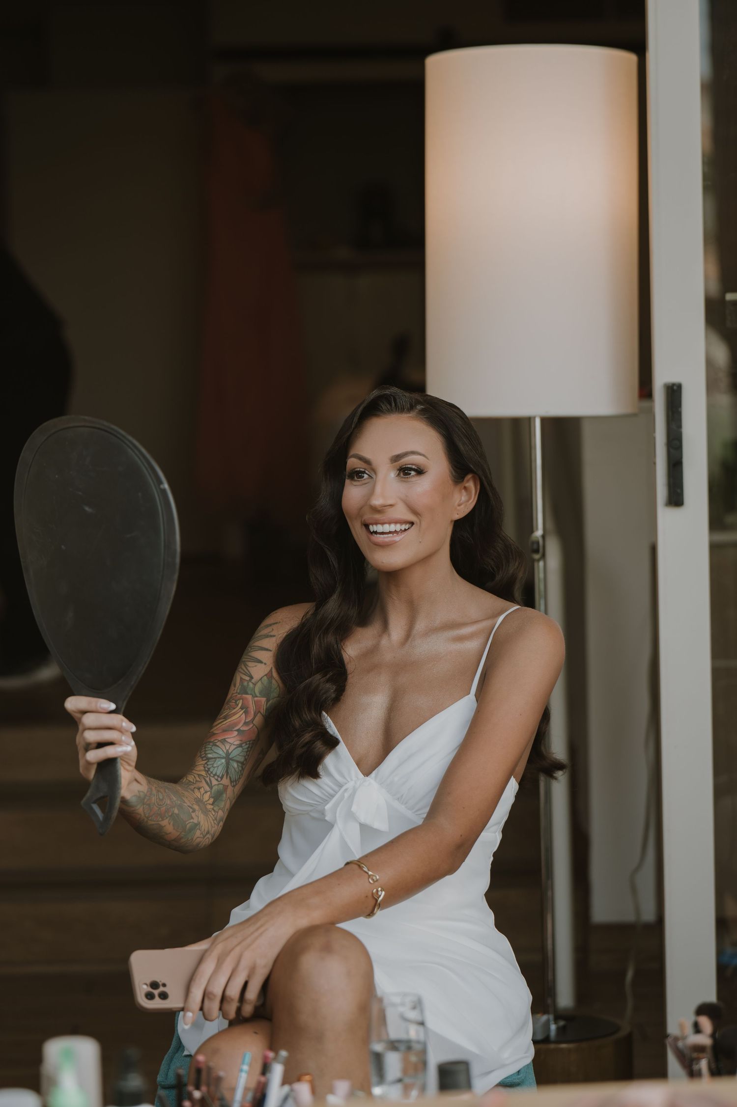 Bride in white dress looking at reflection during wedding preparations.