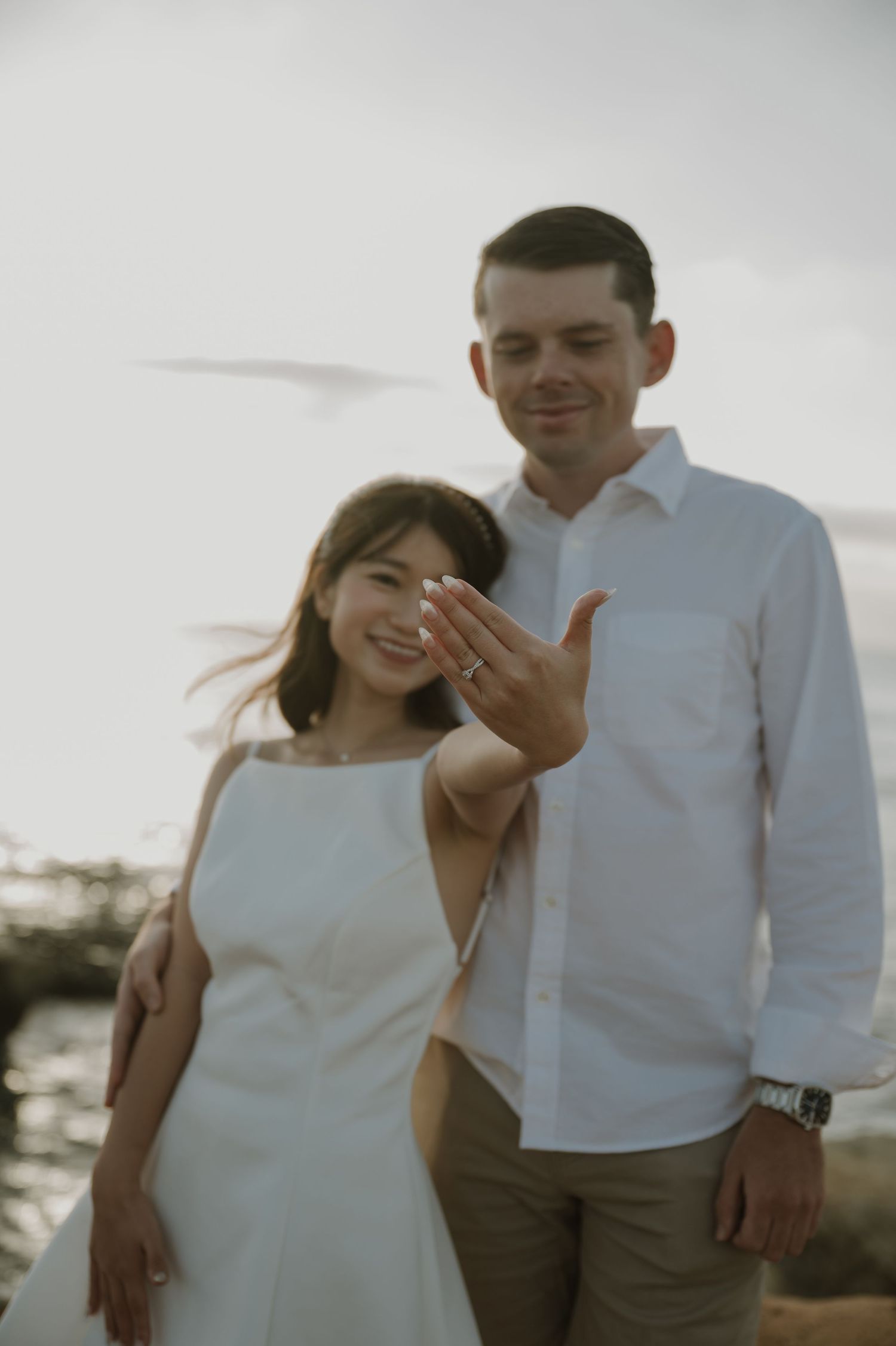 Couple in white and neutral attire sharing intimate moments by the ocean.