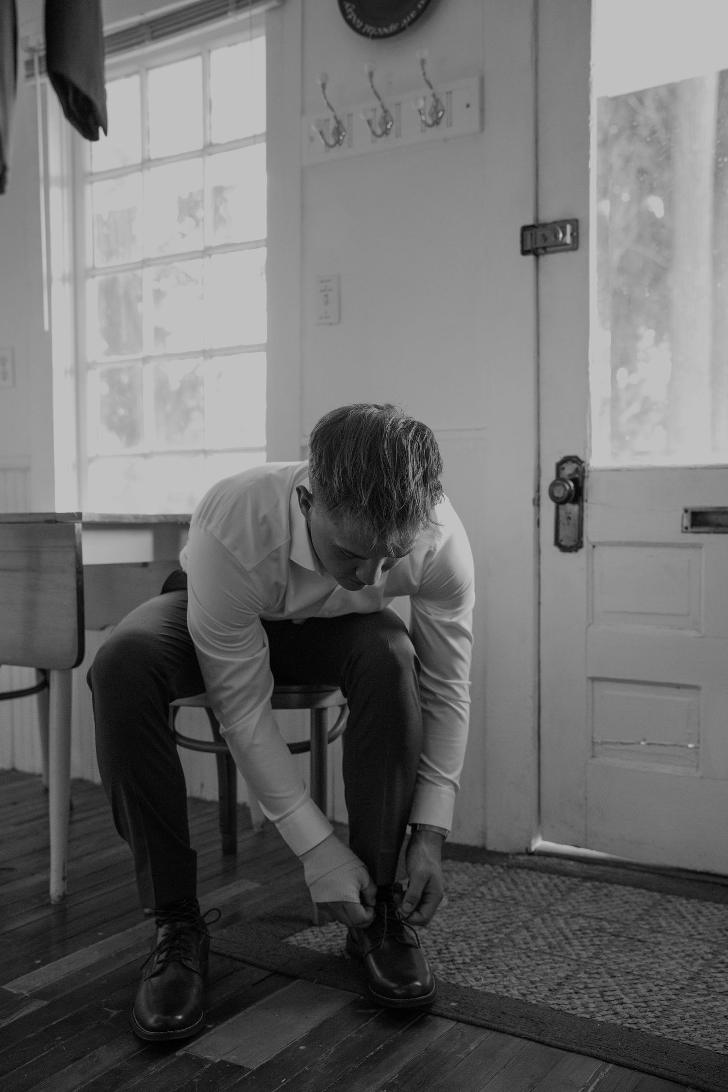 Black and white photo of someone tying dress shoes on a patterned carpet.