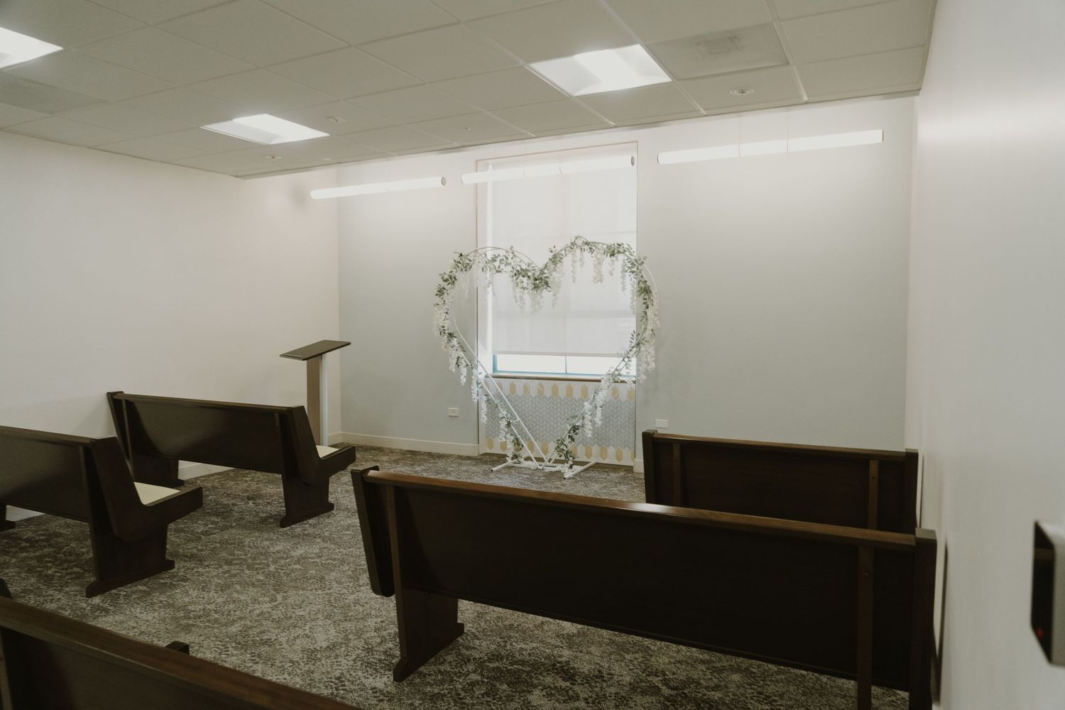 A minimalist white chapel interior with wooden pews and chandelier lighting.