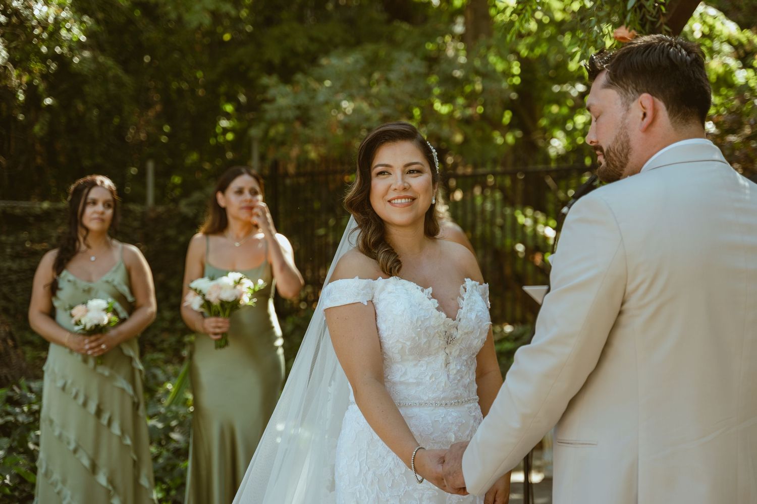 Wedding party poses in sage green bridesmaid dresses against natural outdoor backdrop.