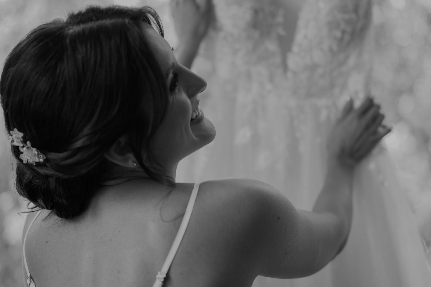 Bride admiring her lace wedding dress in black and white bridal portrait.