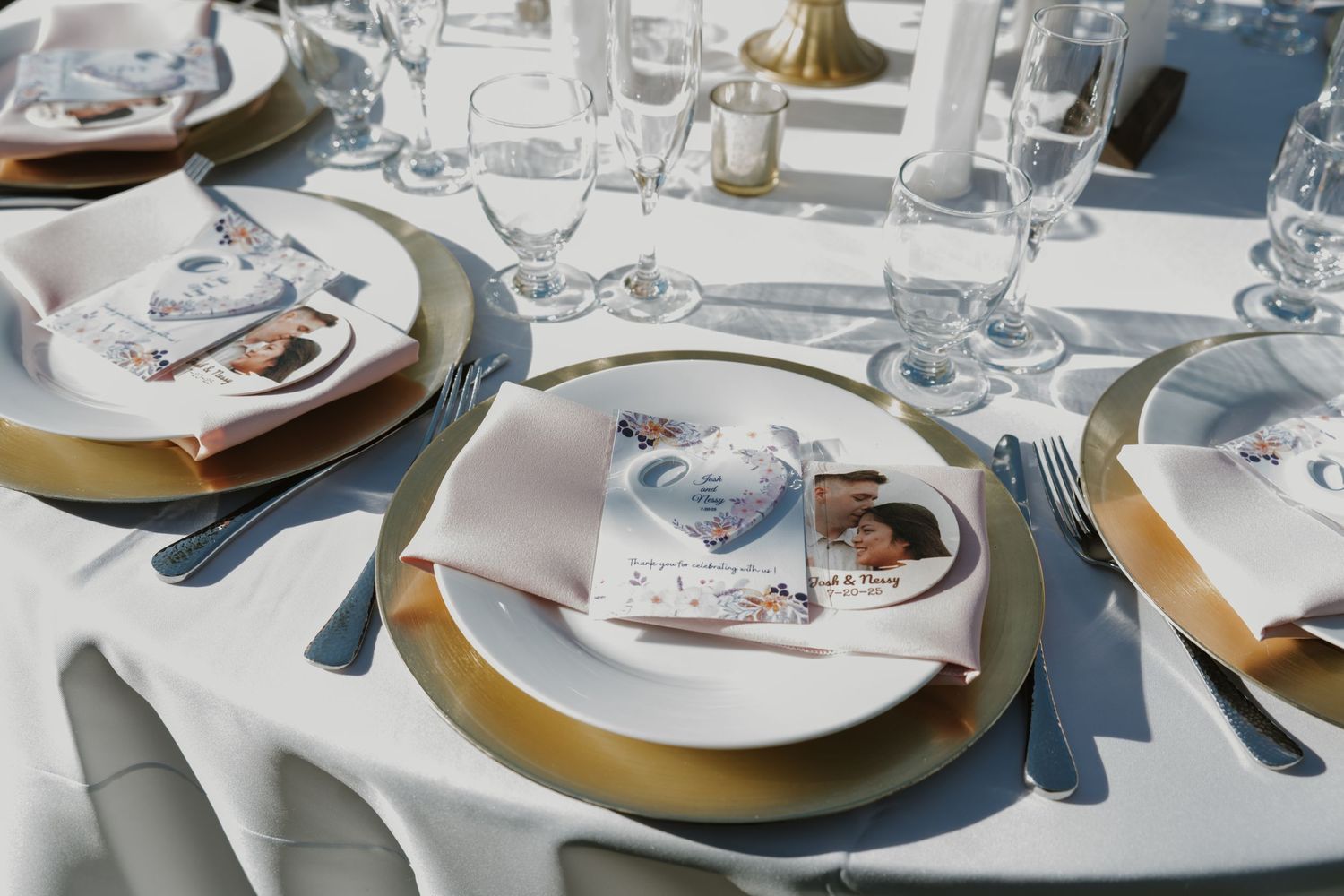 Elegant wedding table setting with gold charger plates, crystal glasses, and personalized photo programs on white linens.