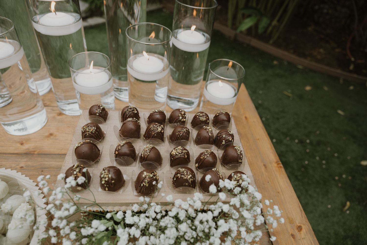 Chocolate truffles displayed on wooden board with floating candle centerpieces and white baby's breath flowers at wedding reception.