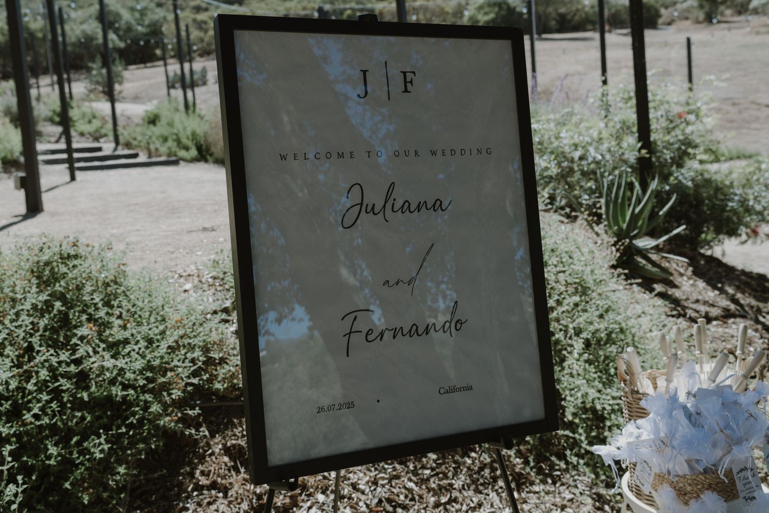 Elegant wedding welcome sign for Juliana and Fernando displayed on an easel in an outdoor garden setting.