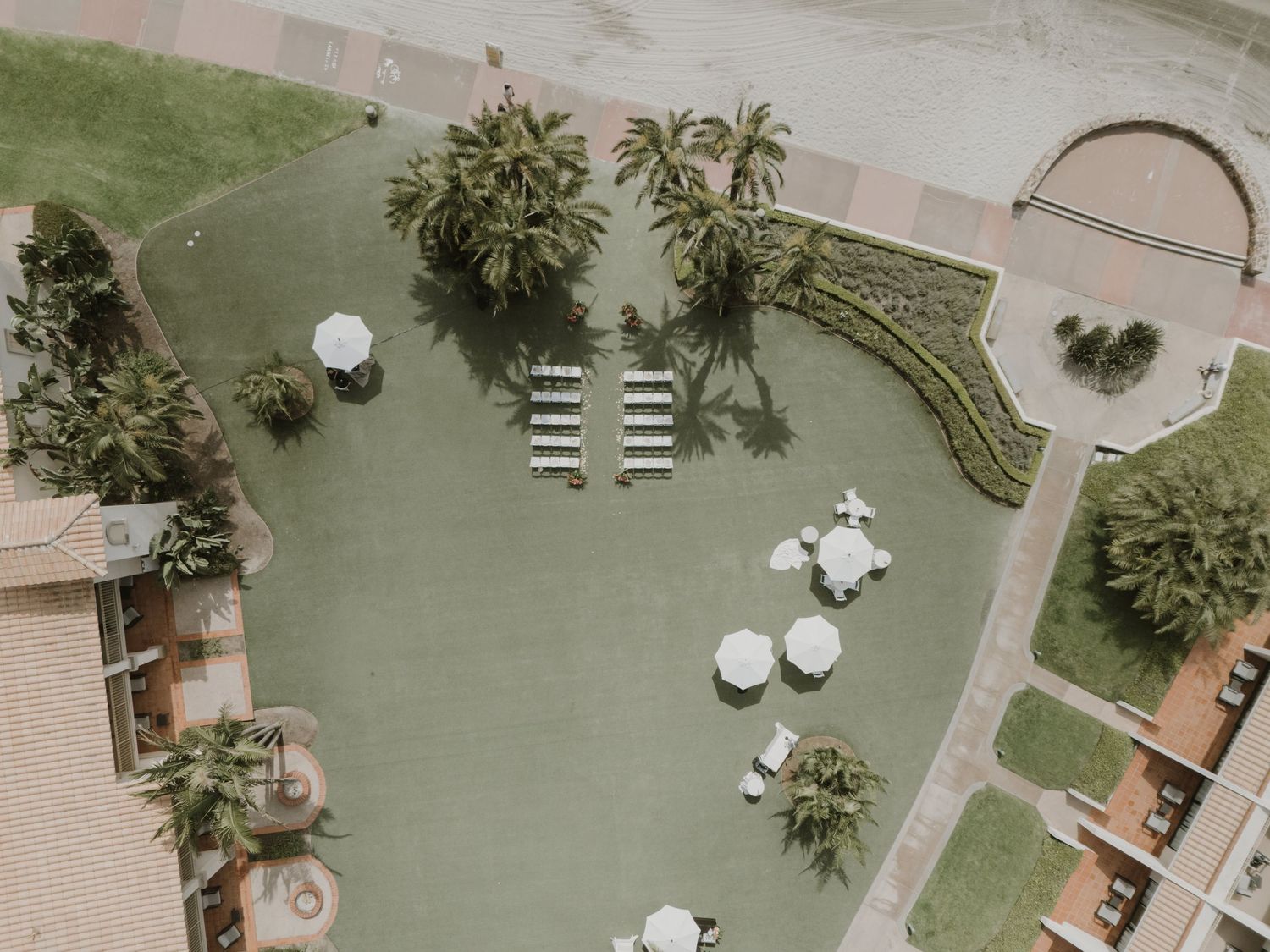 Aerial view of an outdoor wedding venue with white chairs and a decorative arch on manicured grounds.