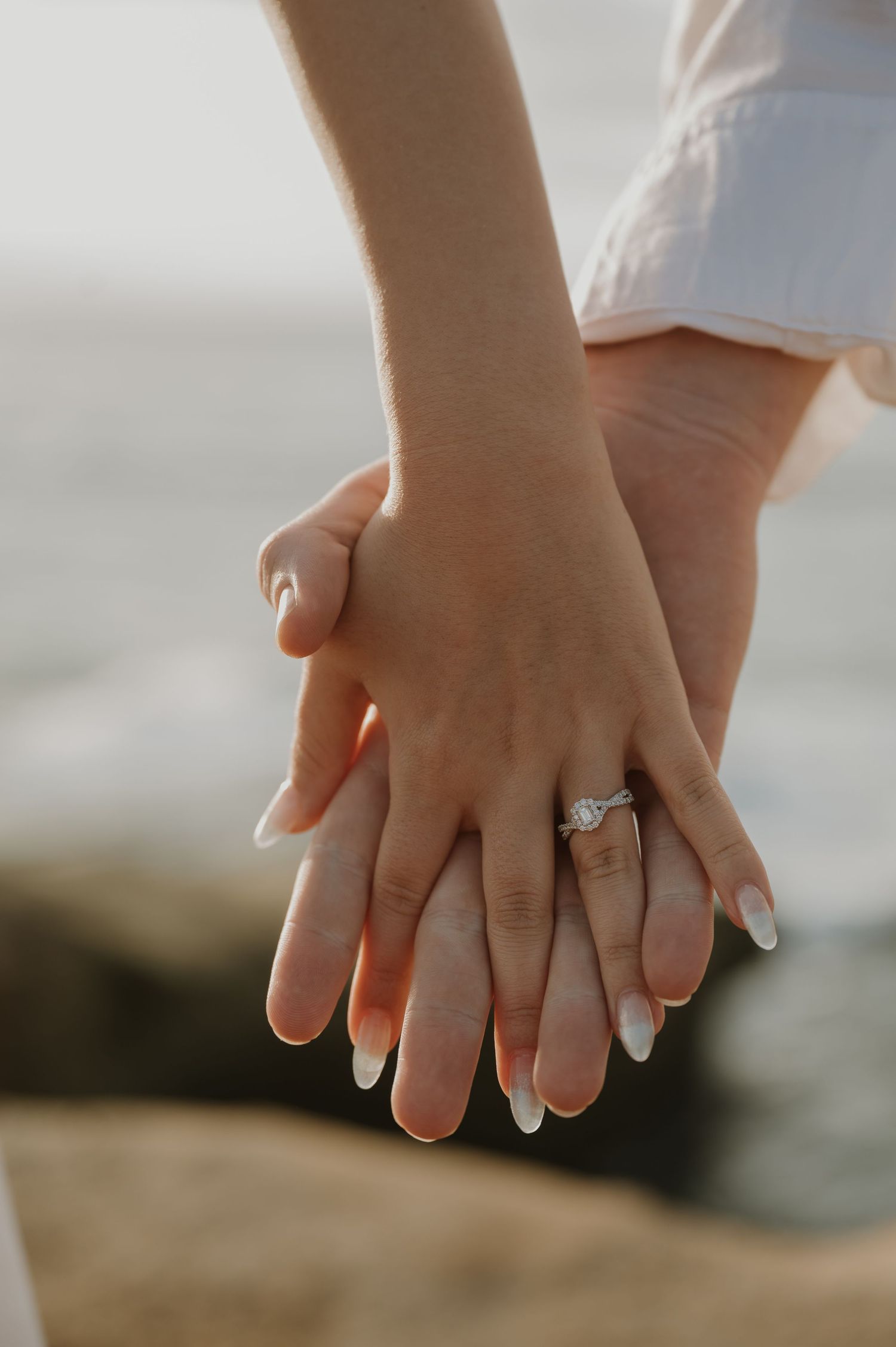 Close-up of hands with engagement rings against a blurred background.