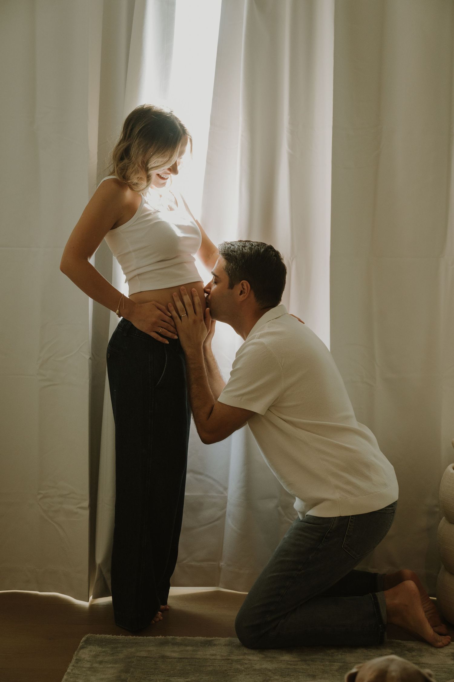 Tender maternity moment captured near window with natural lighting.