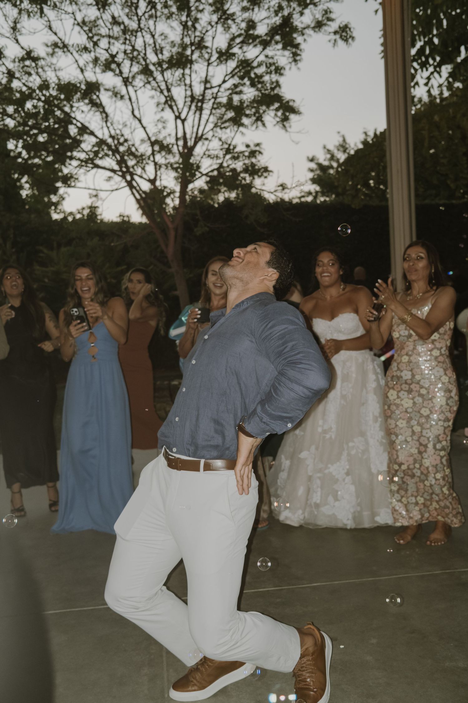 Guest showing off dance moves at outdoor wedding reception as bride and guests cheer.