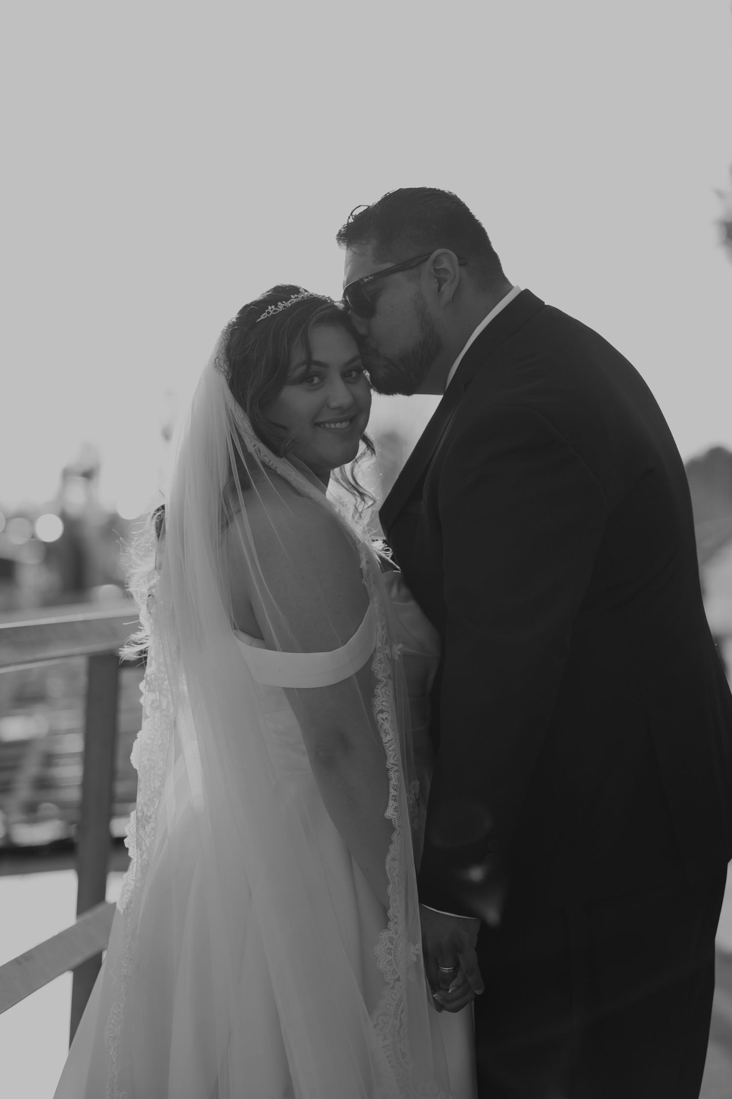 Black and white wedding photo of bride in veil and groom in suit sharing a tender moment outdoors.