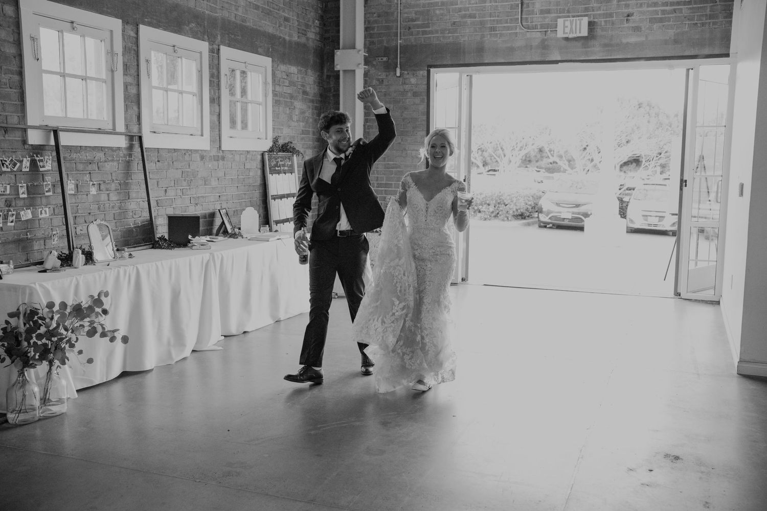 Black and white photo of bride and groom making grand entrance at wedding reception hall.