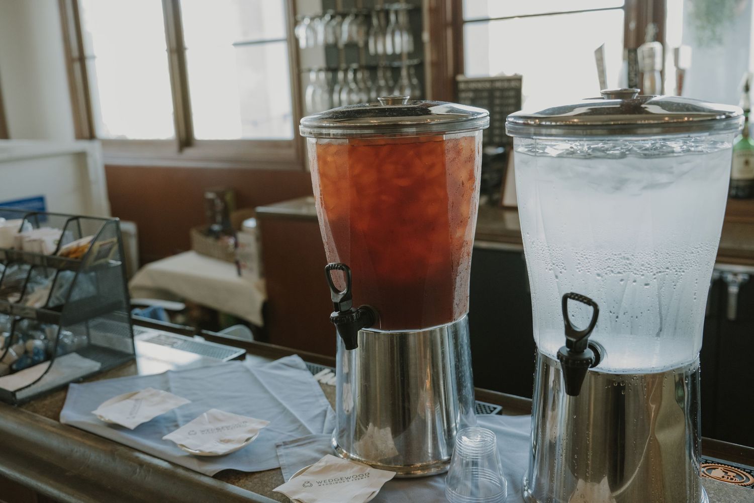 Two glass beverage dispensers filled with iced tea and water on a rustic bar counter at a wedding reception.
