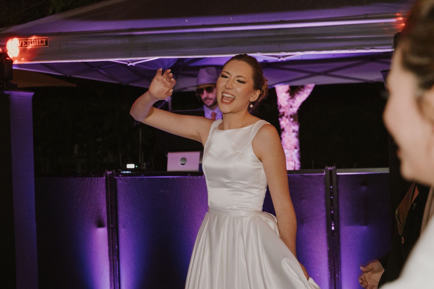 Bride in white dress dancing joyfully near the DJ booth at wedding reception.