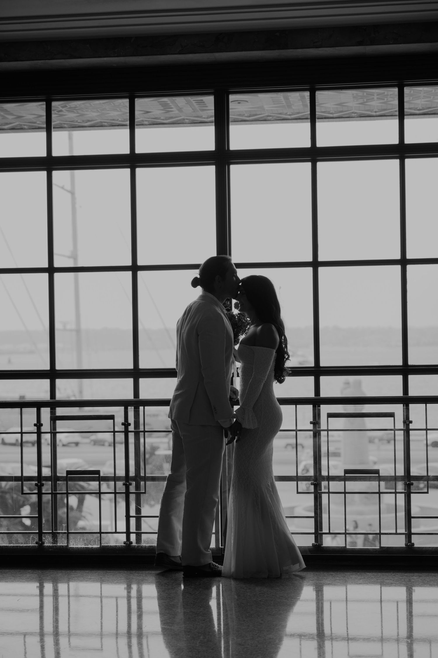 Dramatic silhouettes of wedding couple against large modern windows.