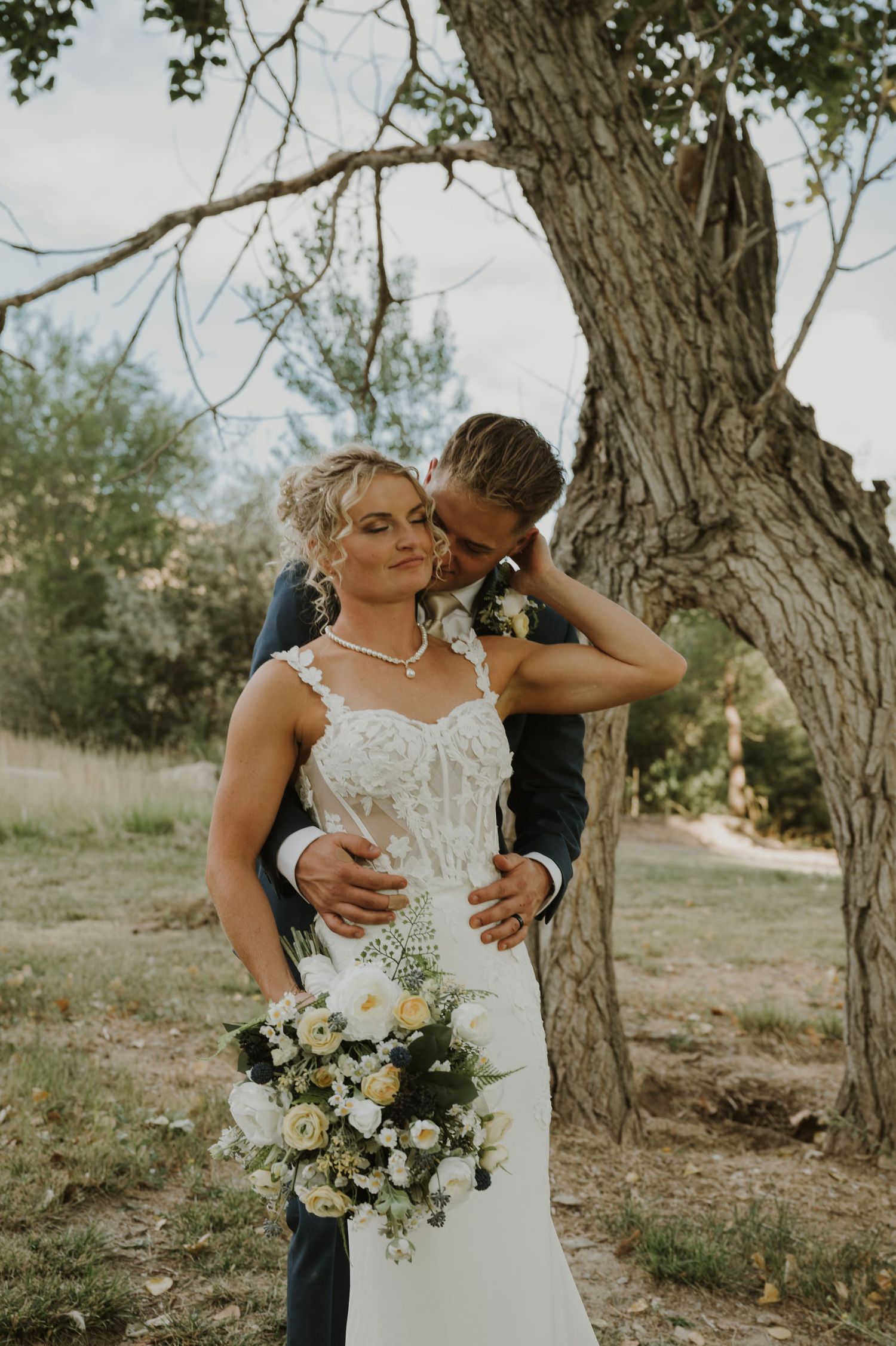 An intimate wedding moment captured in a natural outdoor setting with white flowers.