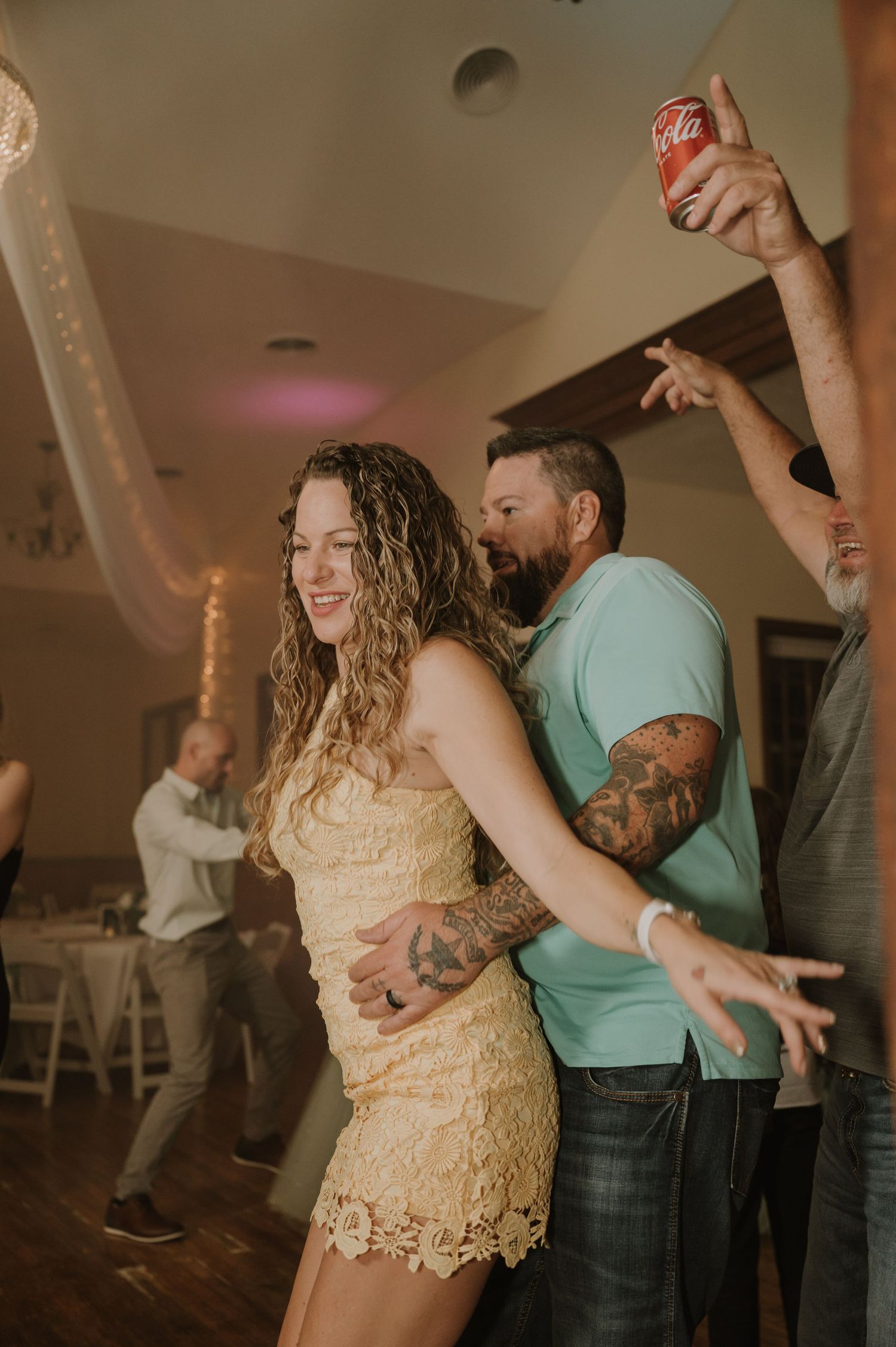 Wedding guests dancing enthusiastically at reception with person holding Coca-Cola can.