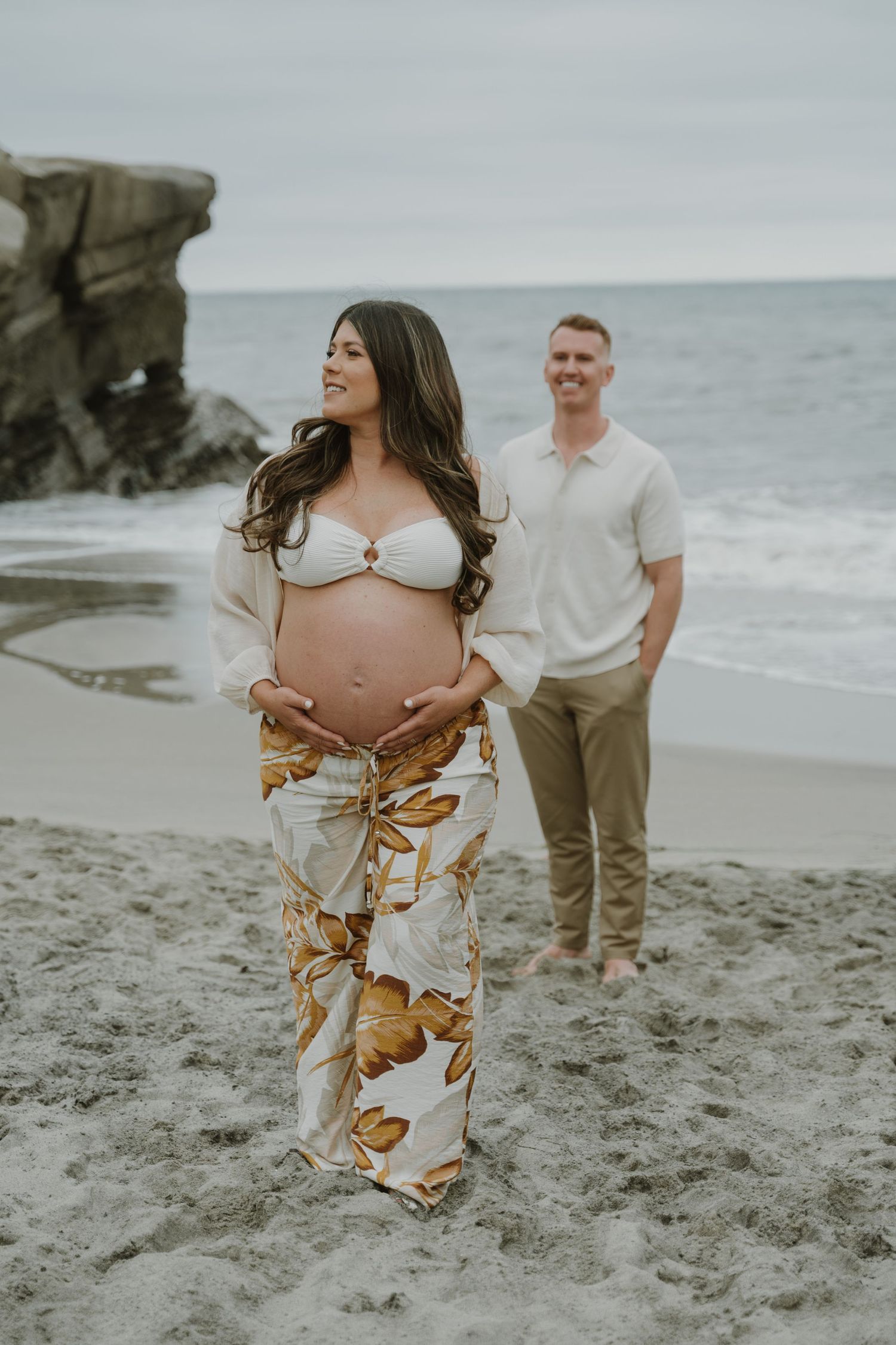 Romantic beach photoshoot featuring a flowing floral dress against a sandy shoreline at sunset.