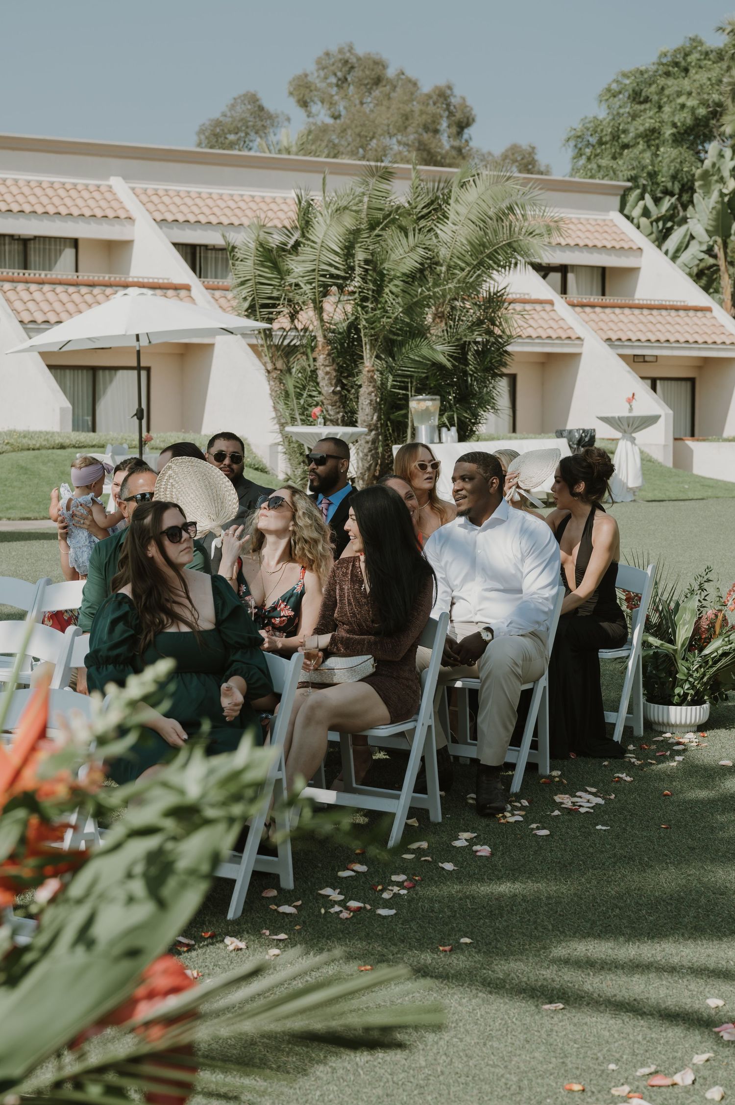 Wedding guests seated in white chairs on lawn for outdoor ceremony.