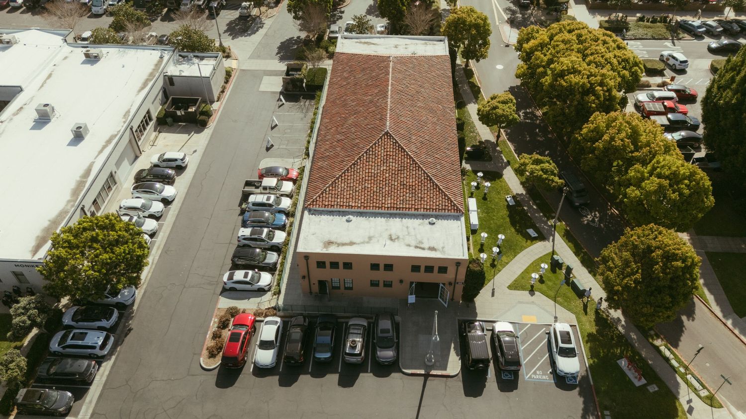 Aerial view of a commercial building with a red tile roof surrounded by a parking lot and trees.